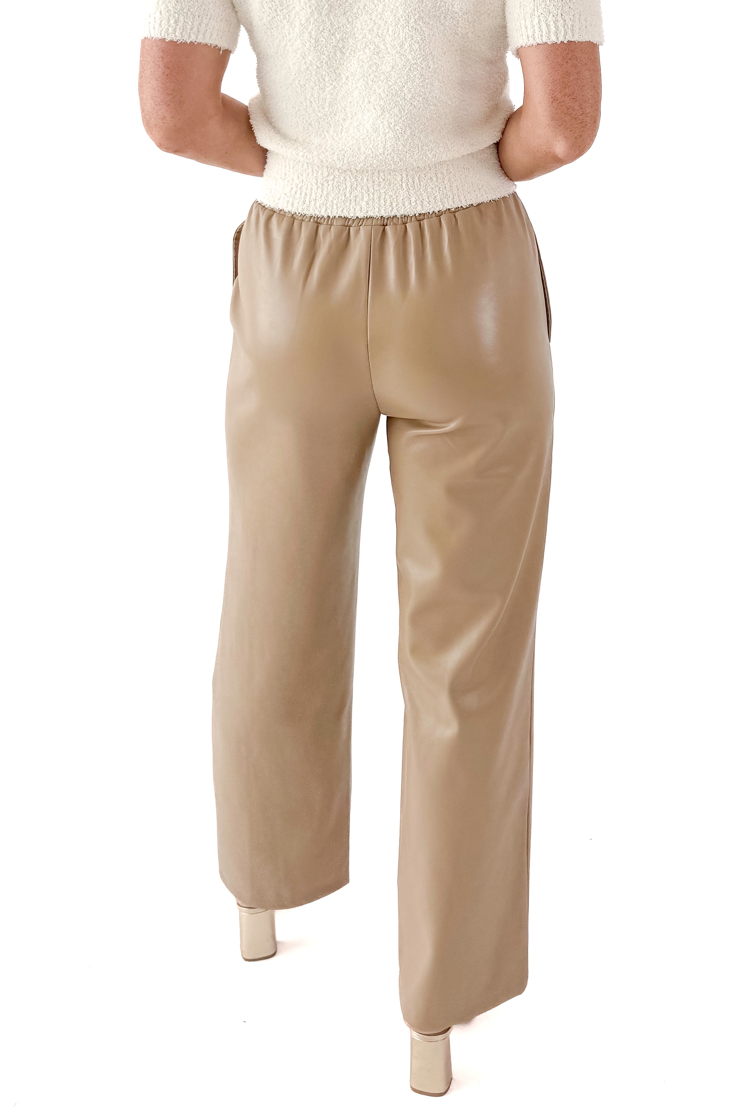 Back view of woman wearing Macchiato Faux Leather Pants and sweater against white studio background.