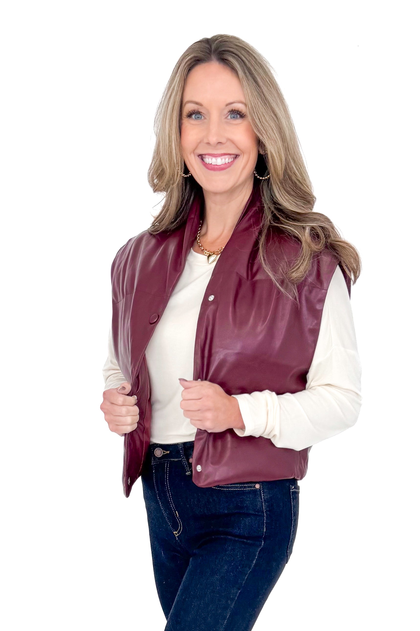 Front view of woman wearing plum faux leather vest with jeans against white studio background.