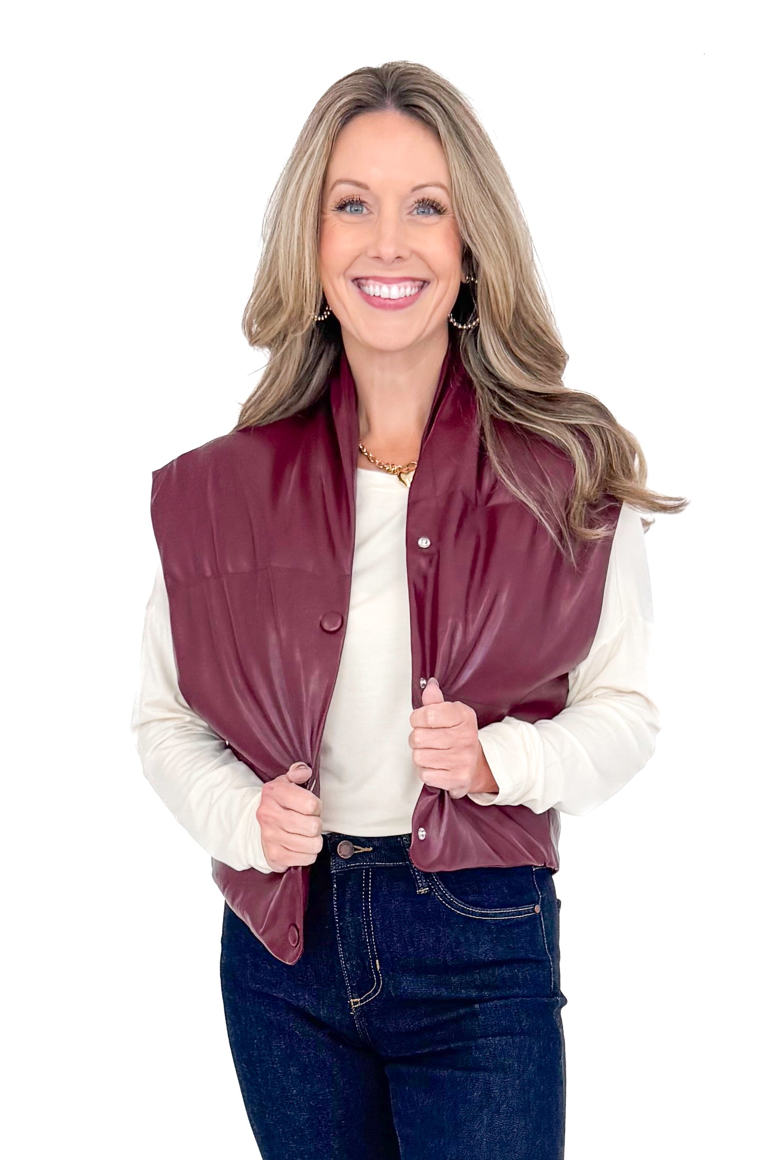 Front view of woman wearing plum faux leather vest with jeans against white studio background.
