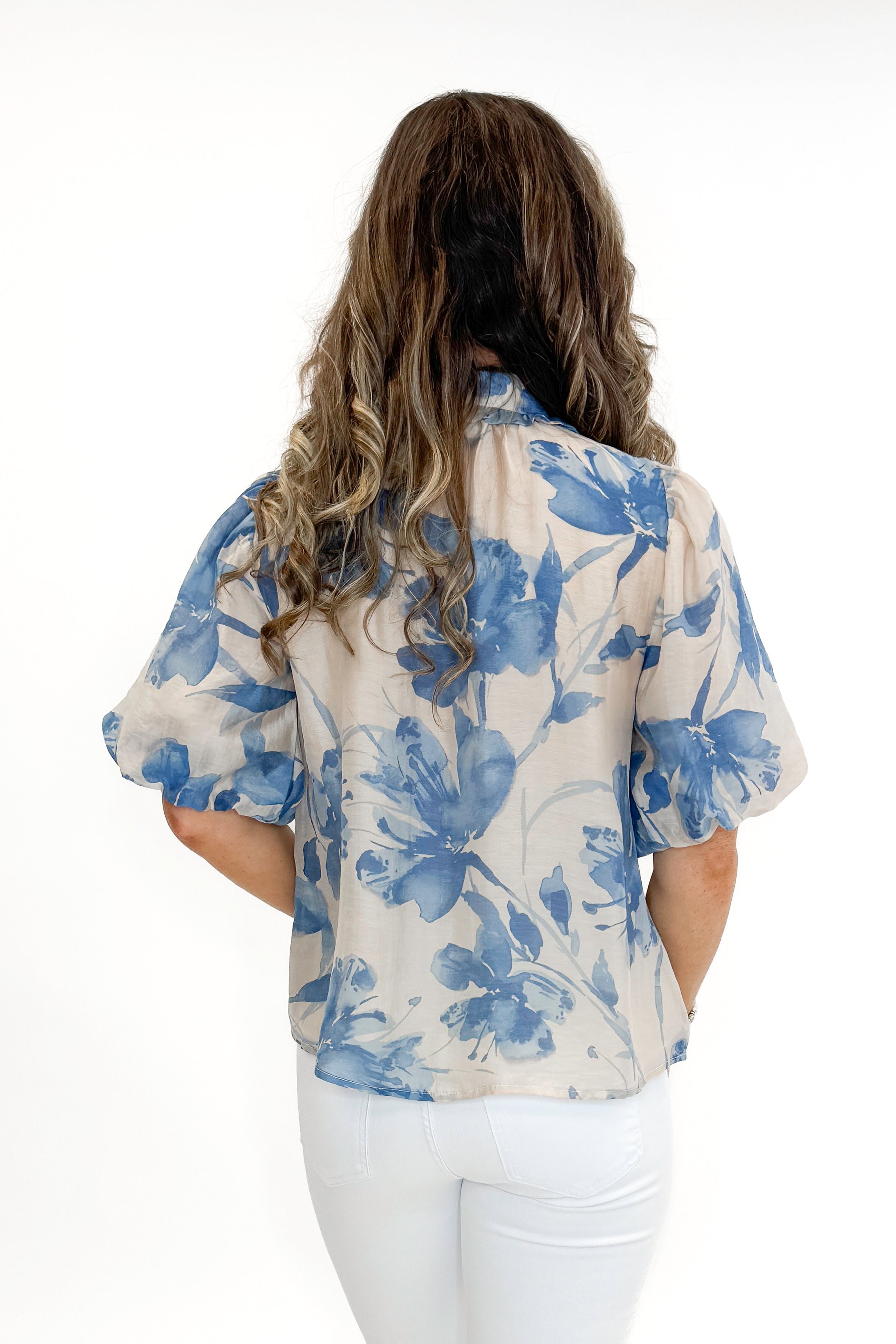 Back view of woman wearing Cream & Blue Floral Neck Tie Detail Top by Fate with white jeans against white studio background.