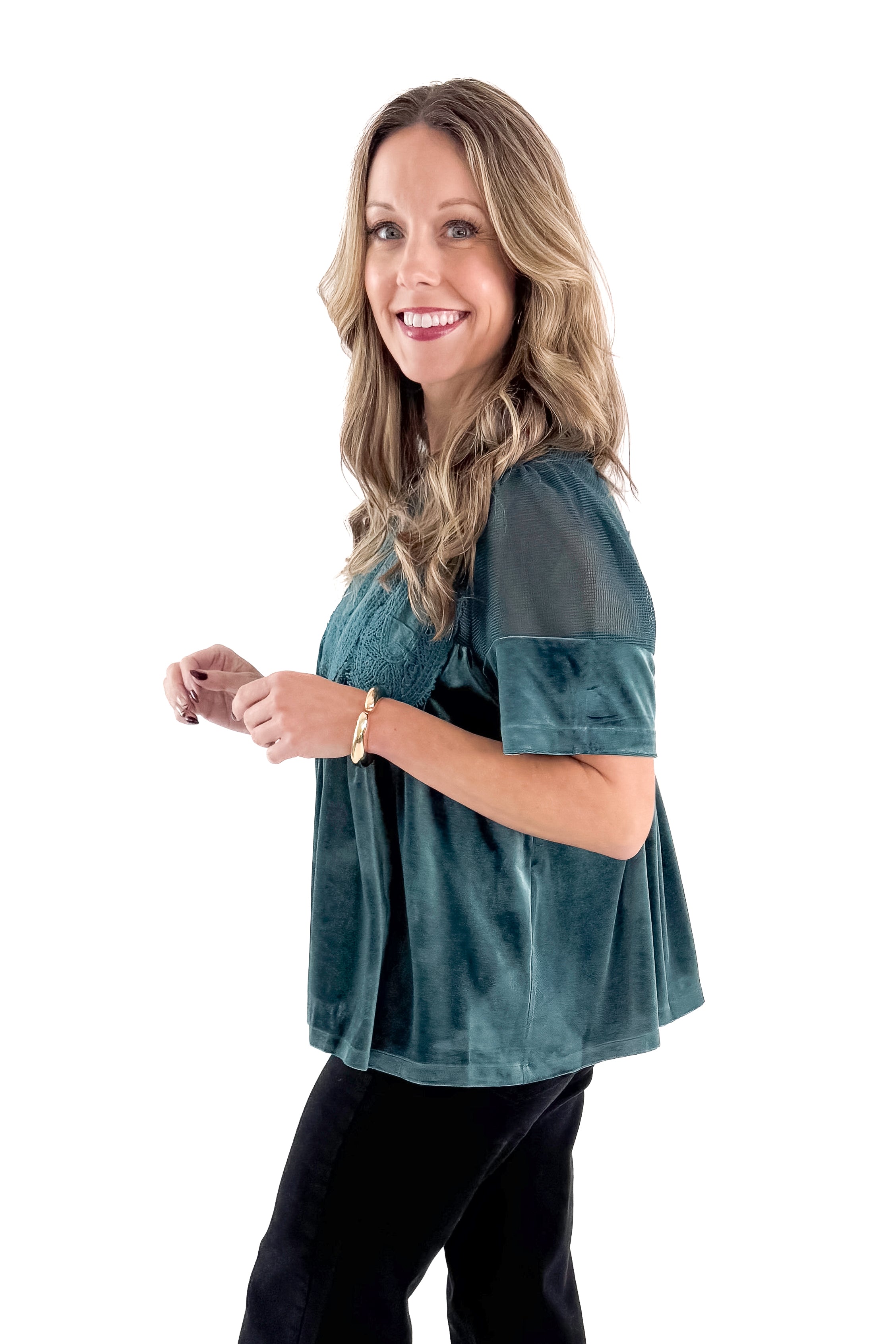 Side view of woman wearing Teal Velvet With Lace Applique Top with jeans against white studio background.