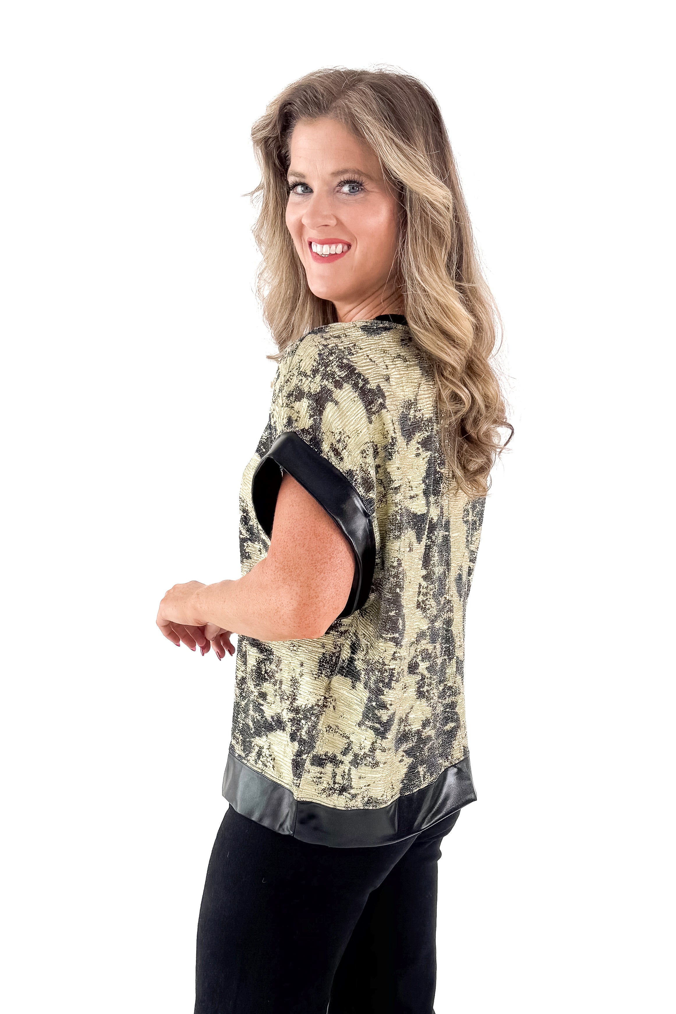 Side view of woman wearing Black & Gold Metallic Abstract Print Top with jeans against white studio background.