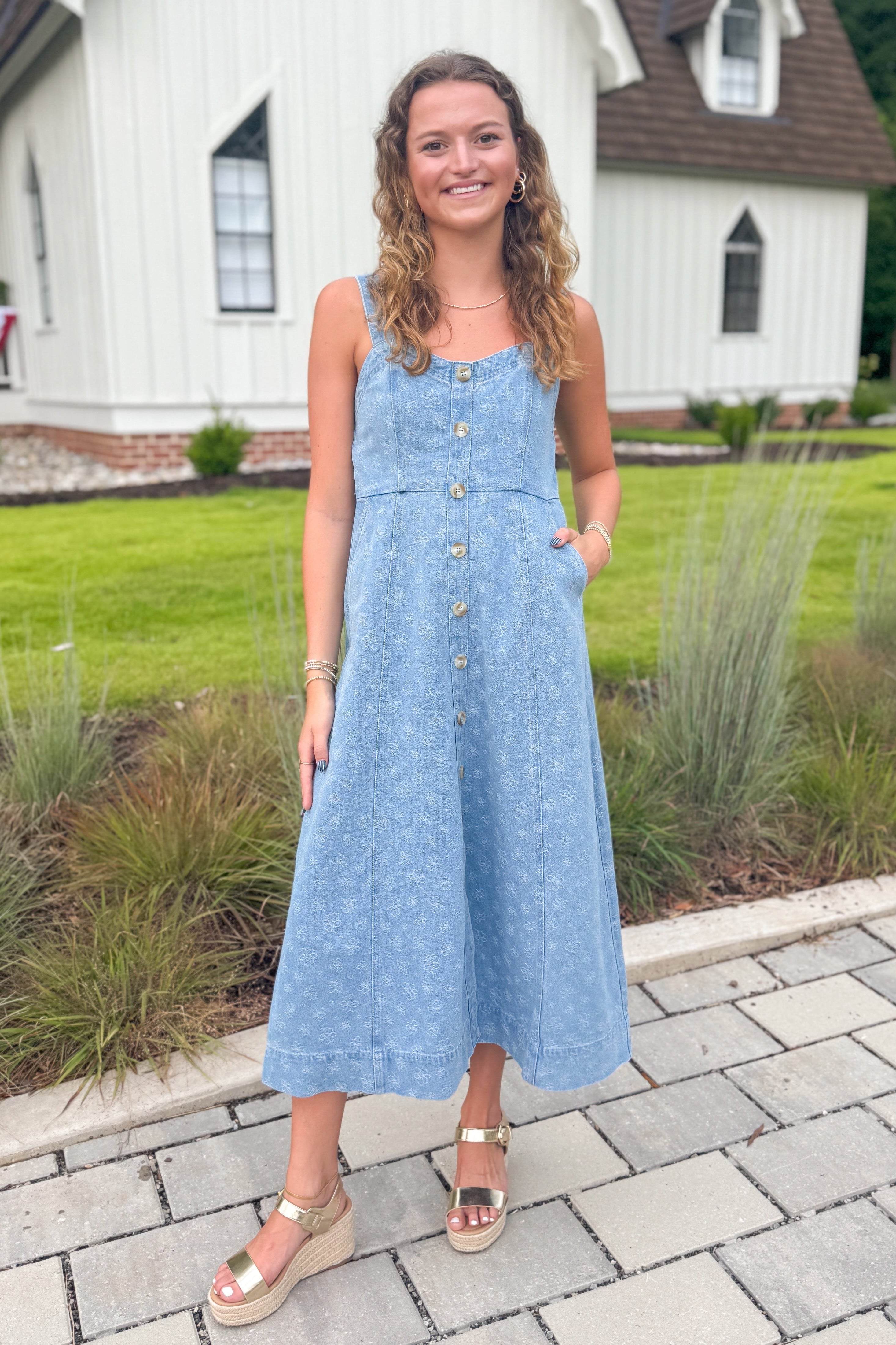 Front view of woman wearing Swagger Boutiqueās Denim Floral Textured Midi Dress with sandals walking down a path.