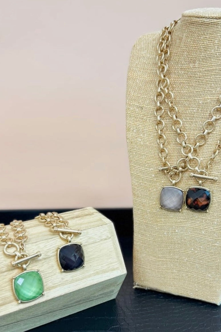 Jewelry set with gemstone pendants on a beige stand and wooden display block.
