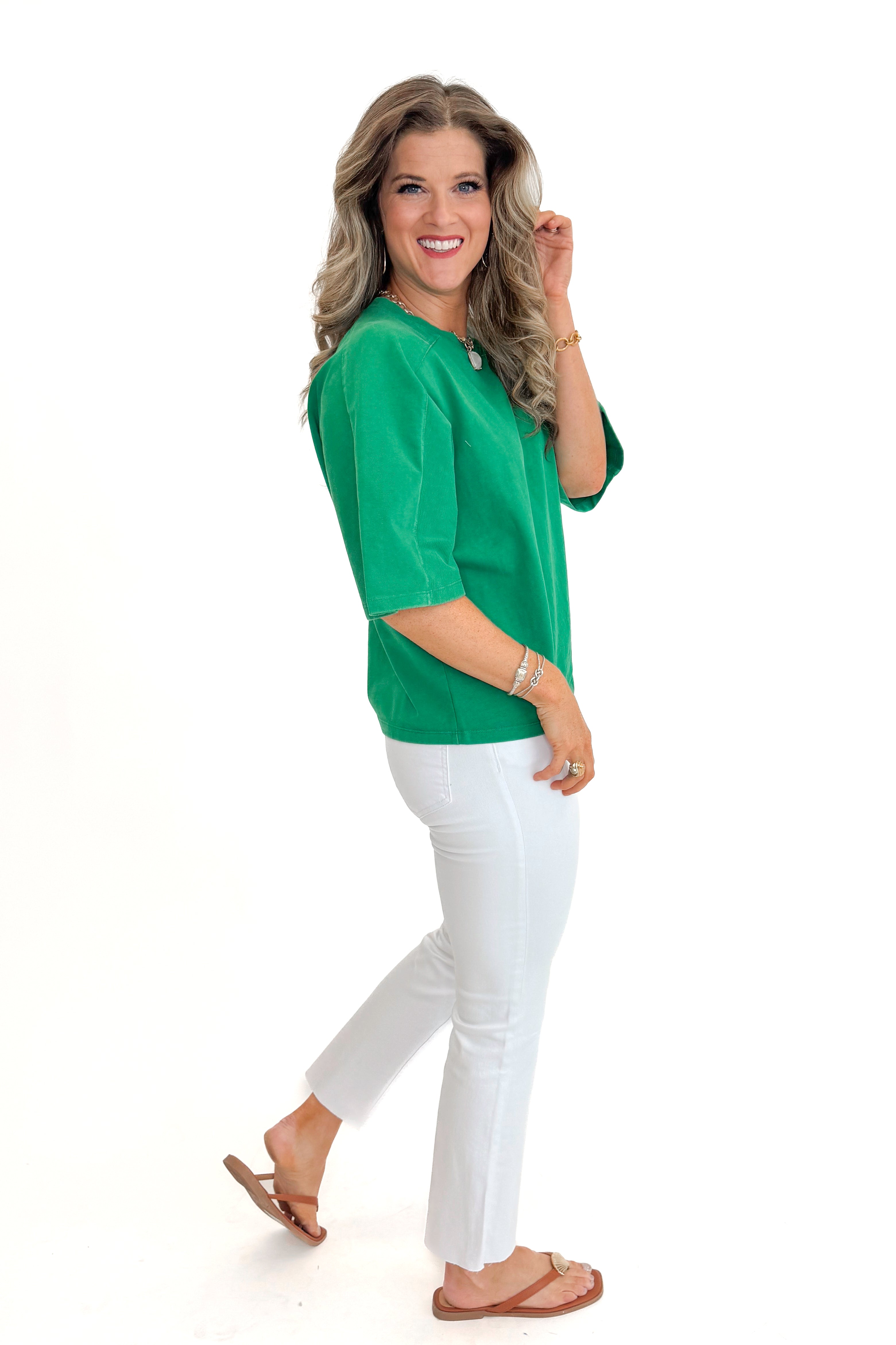 Side view of woman wearing Green Washed Boxy Tee with jeans against white studio background.