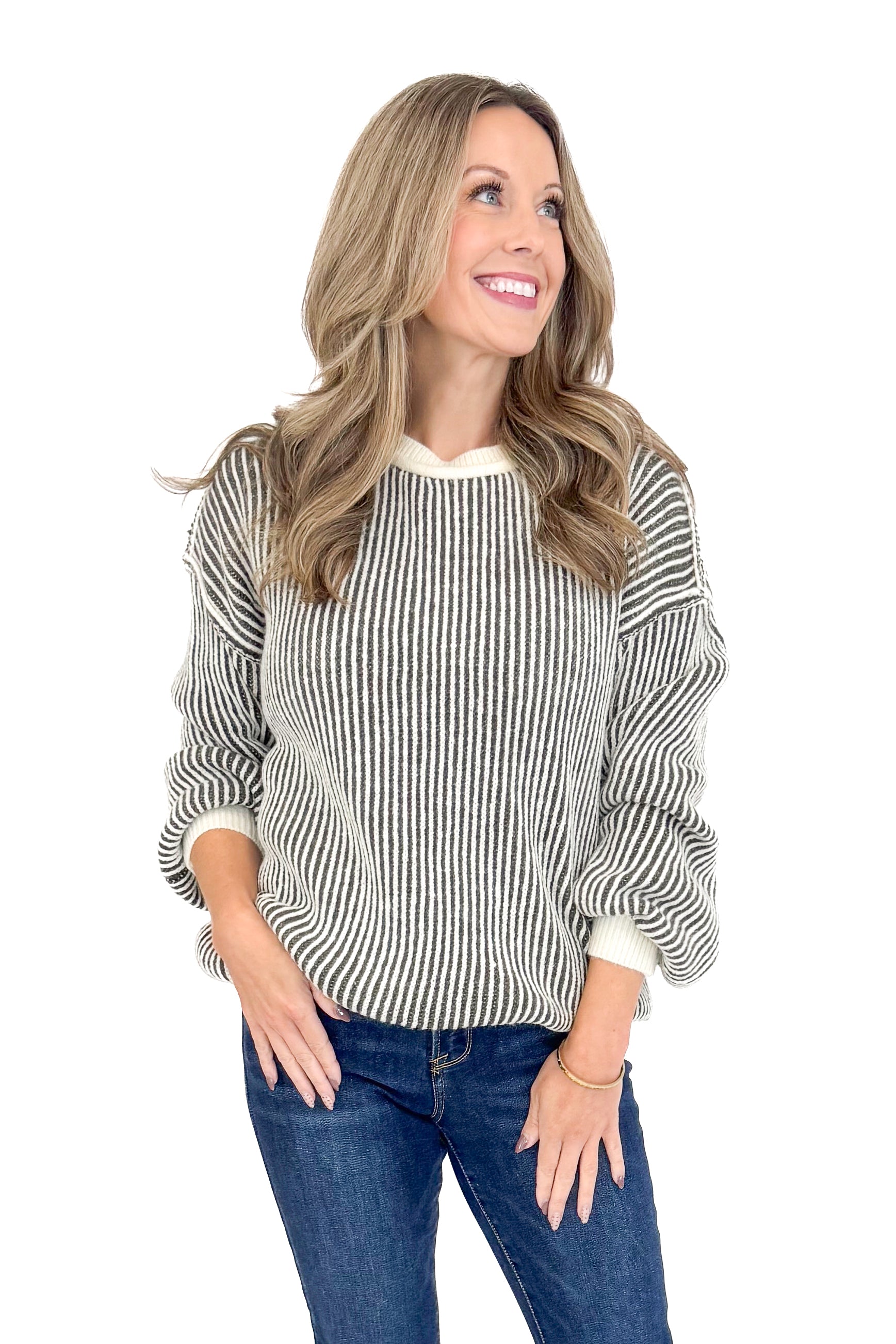 Front view of woman wearing Cream and Charcoal Striped Sweater with jeans against white studio background.