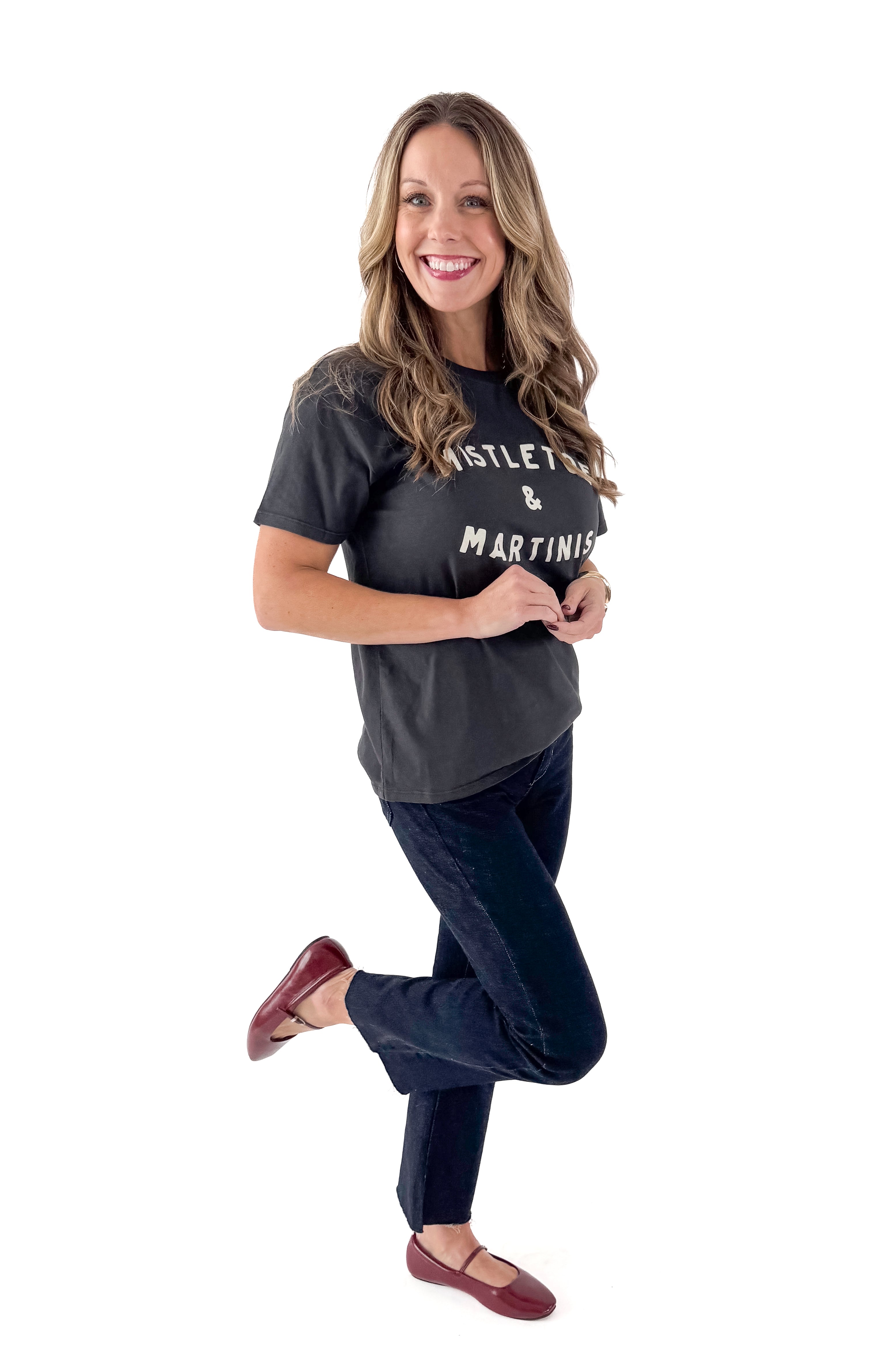 Side view of woman wearing Mistletoe Z Supply tee with jeans against white studio background.
