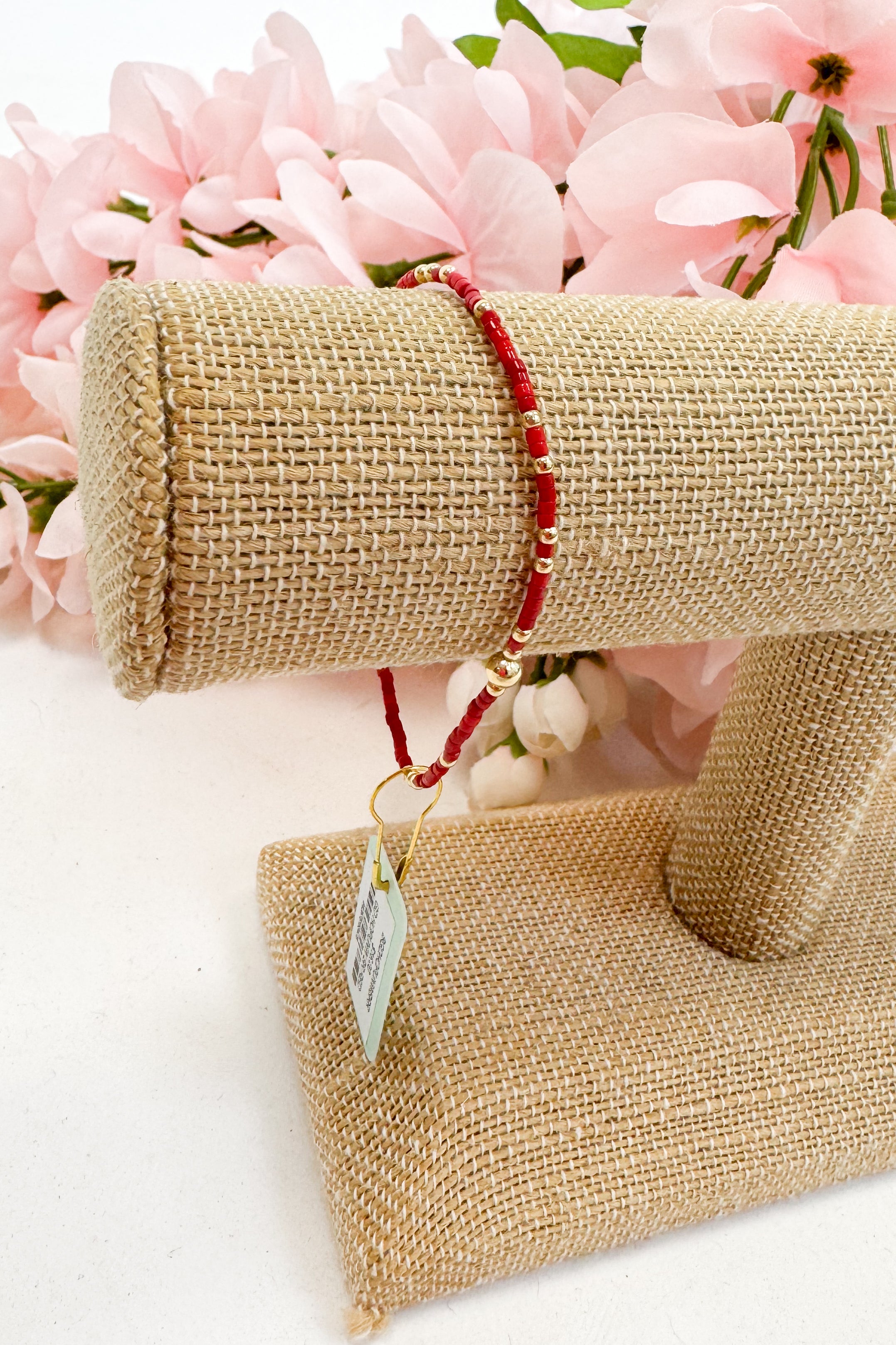 Red bracelet on a burlap roll with pink flowers in the background