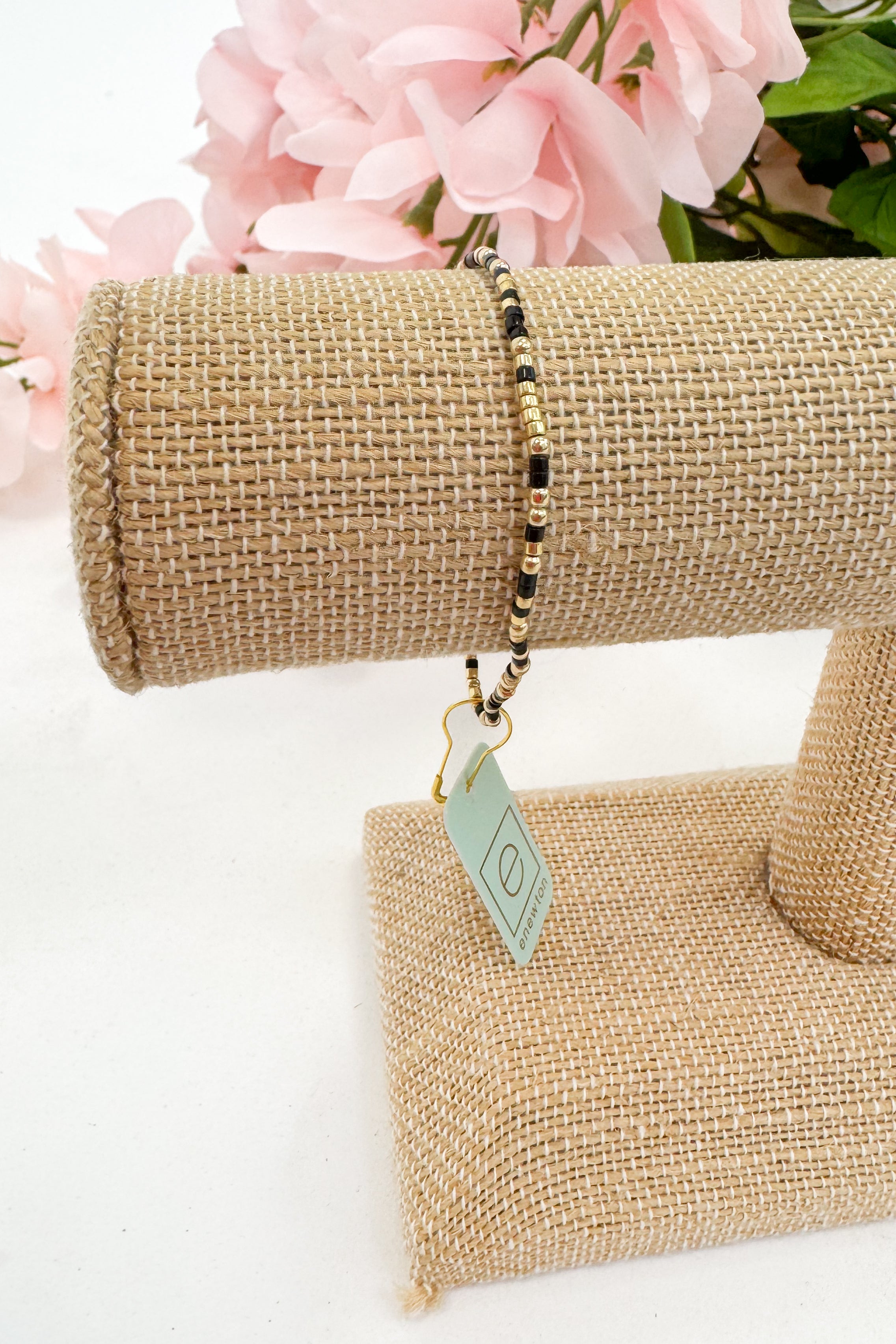 Bracelet on a burlap stand with pink flowers in the background