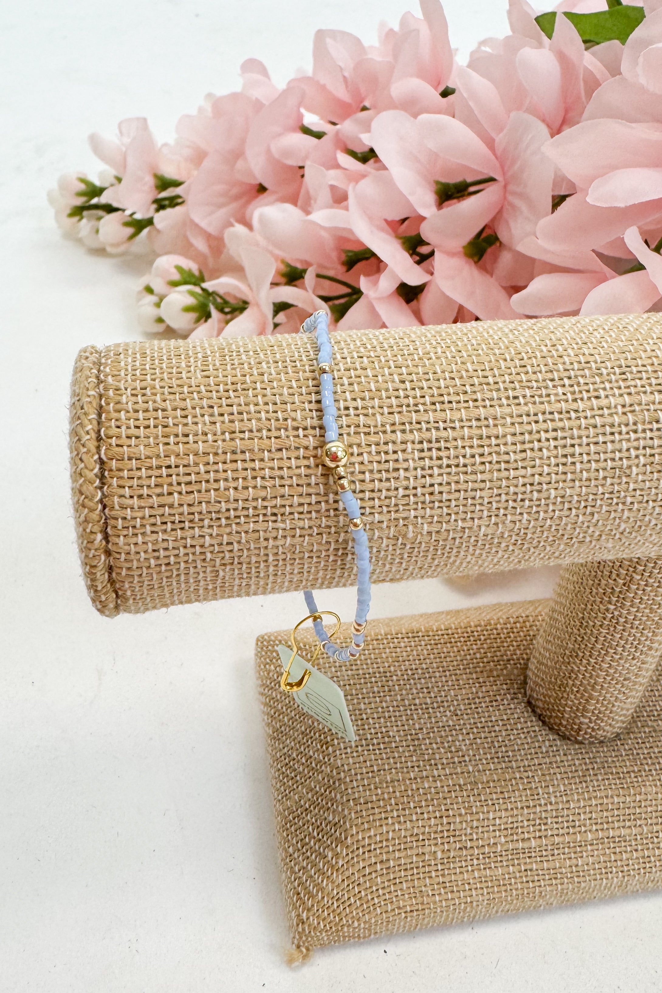 light blue bracelet on a beige jewelry display with pink flowers in the background