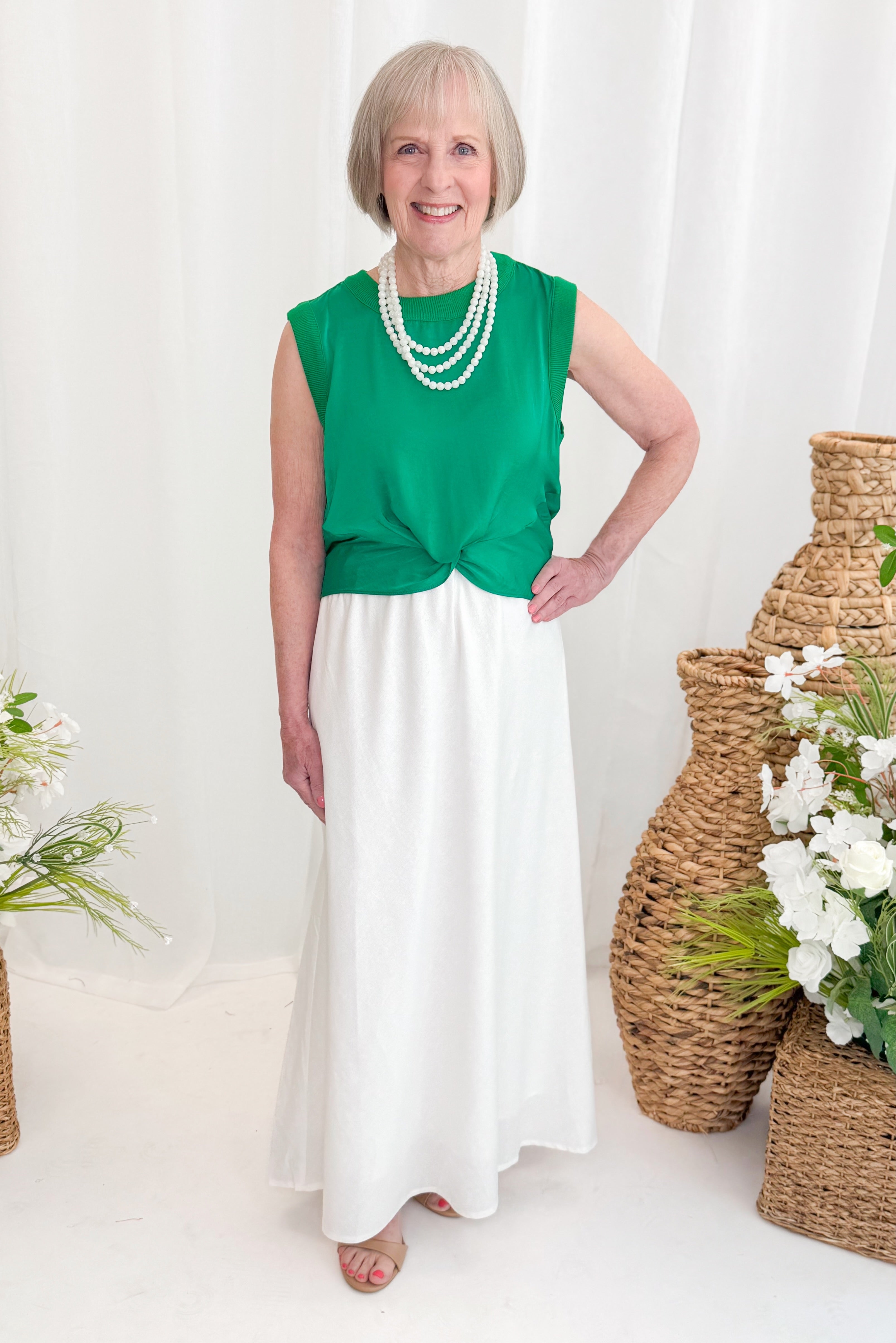 Front view of woman wearing Swagger Boutique’s Green Sleeveless Tank With Twist by Skies Are Blue with white skirt at boutique.