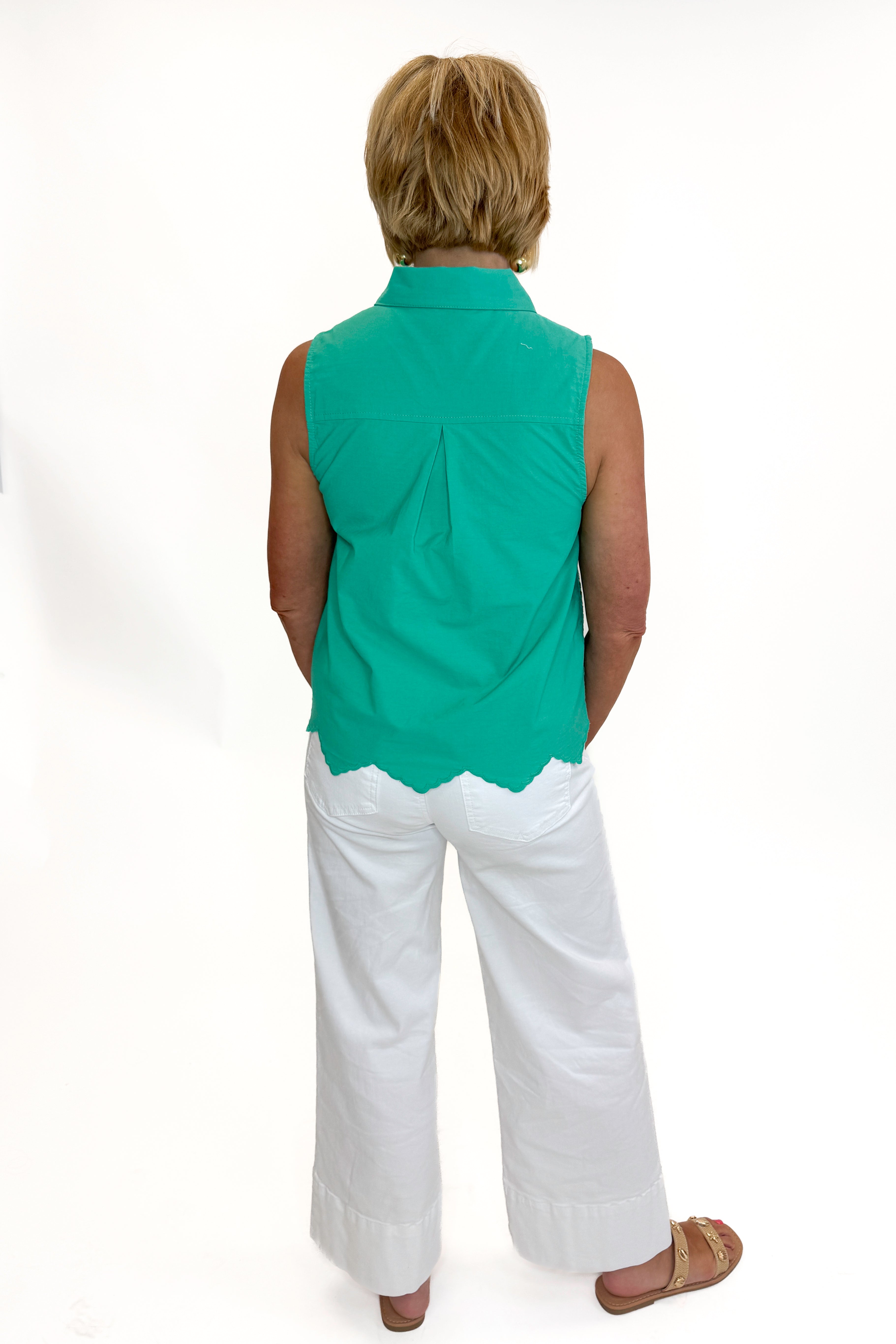 Back view of woman wearing Swagger Boutiqueβs Green Tie Neck Eyelet Sleeveless Top with jeans against white studio background.