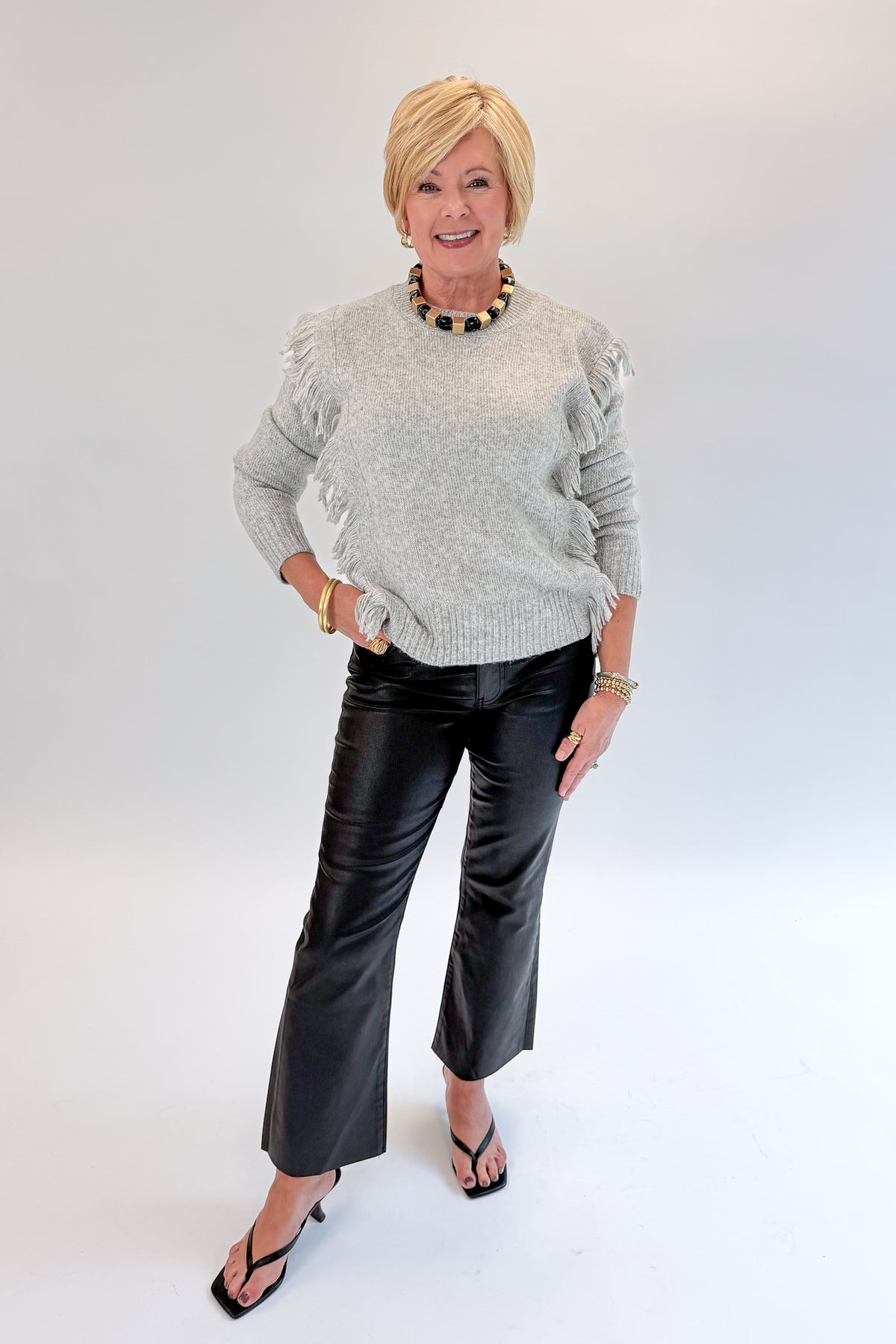 Front view of woman wearing Swagger Boutique’s Grey Fringe Sweater with jeans against white studio background.