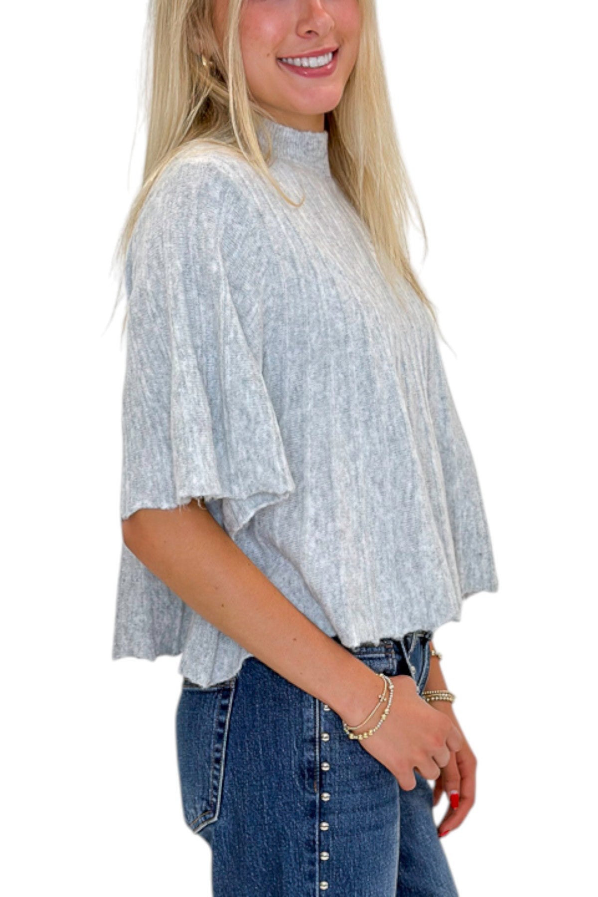 Side detail view of woman wearing Swagger Boutiqueās Grey Ribbed Short Sleeve Sweater with jeans against white studio background.