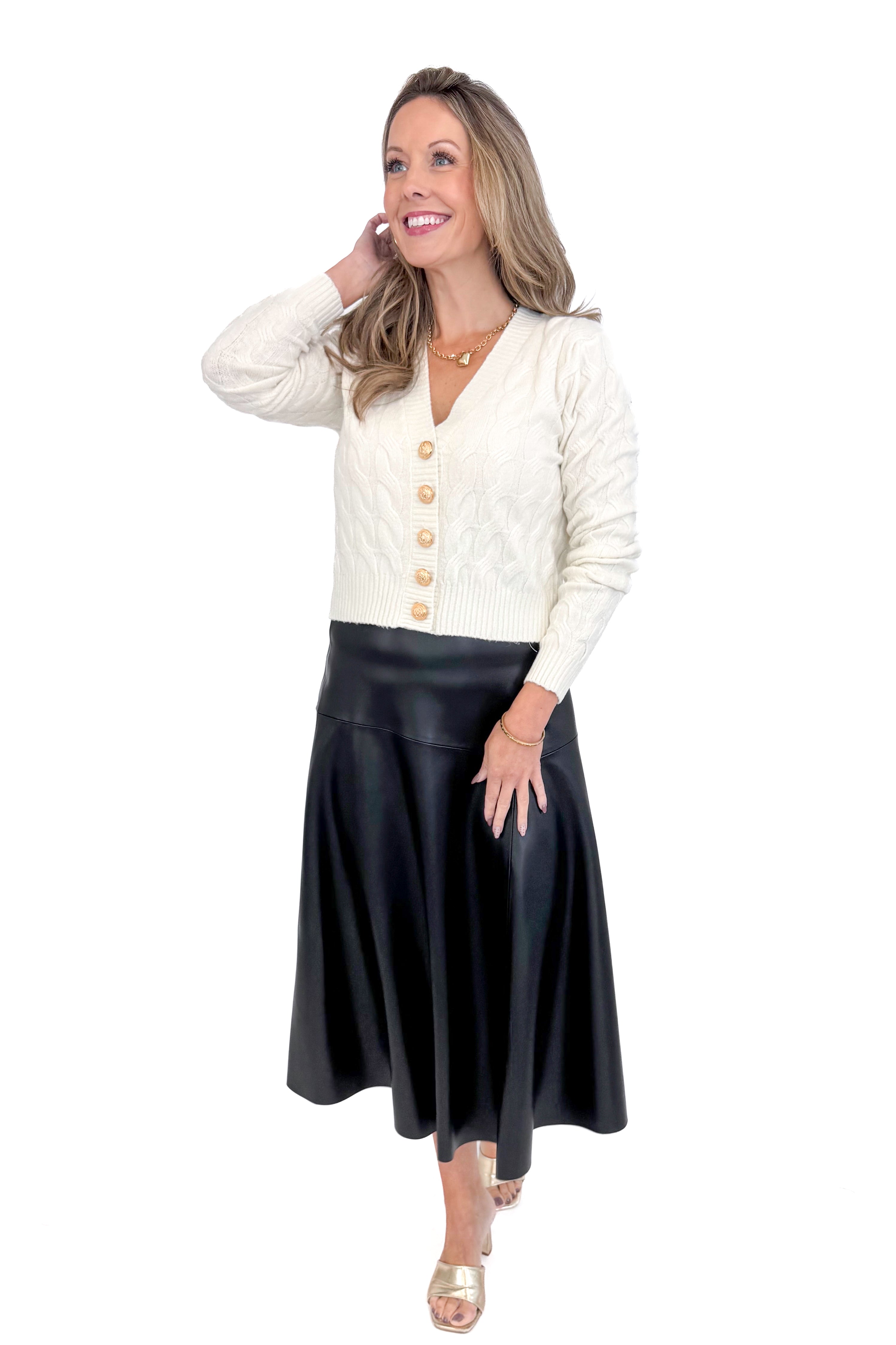 Front view of woman wearing Cream Cable Knit Button Up Cardigan with black skirt against white studio background.