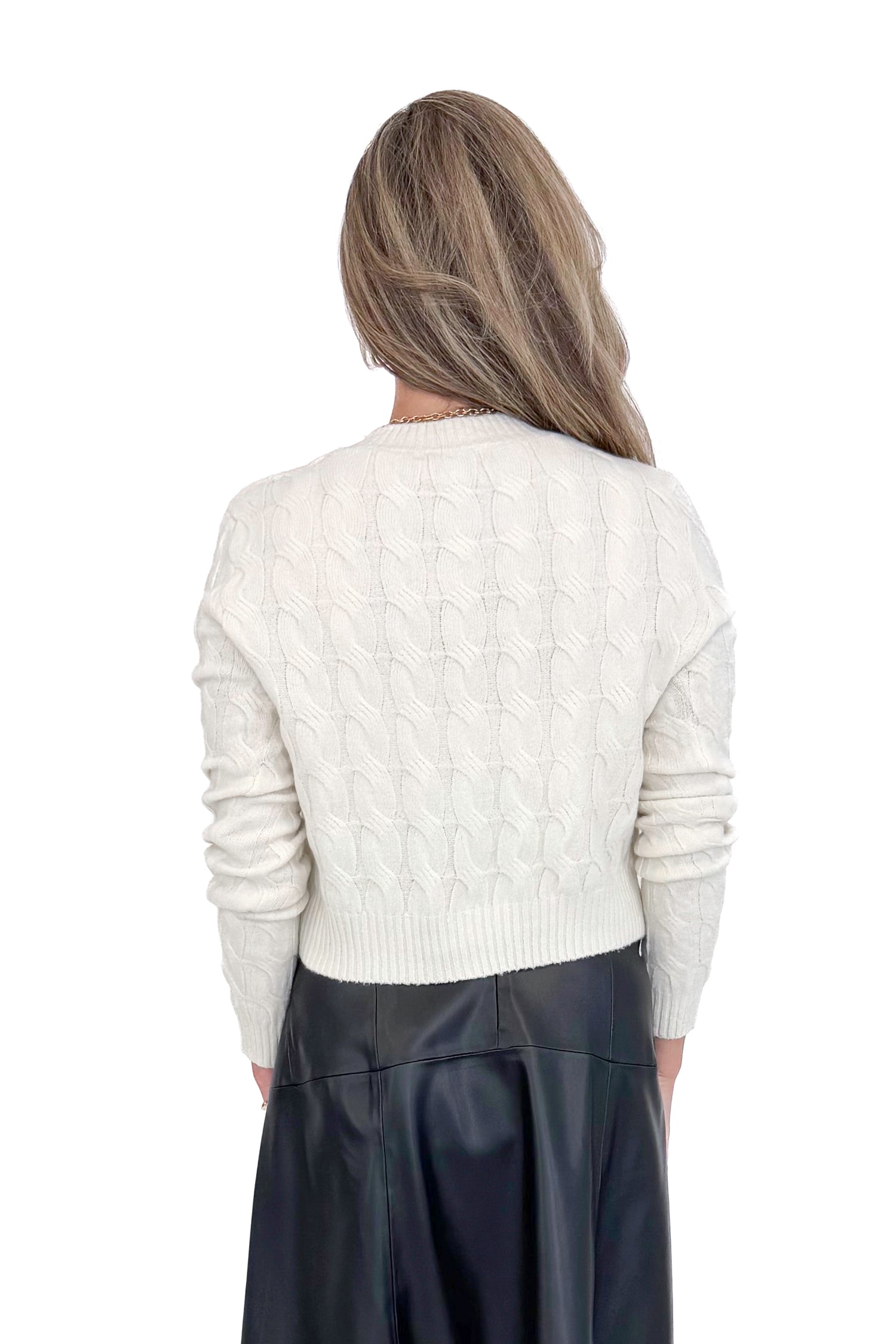 Back view of woman wearing Cream Cable Knit Button Up Cardigan with black skirt against white studio background.