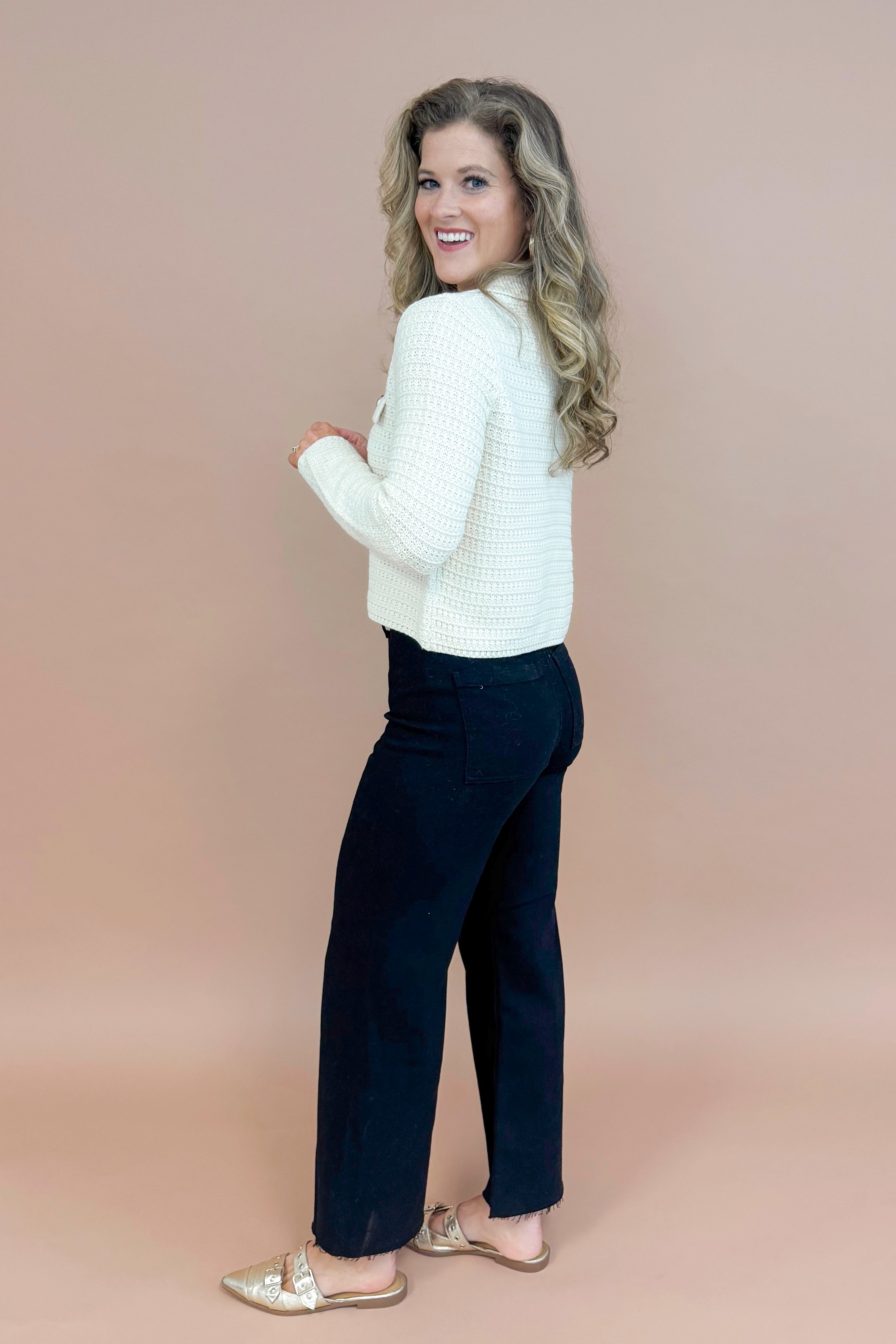 Side view of woman wearing Cream Textured Button Up Cardigan and jeans with taupe background.