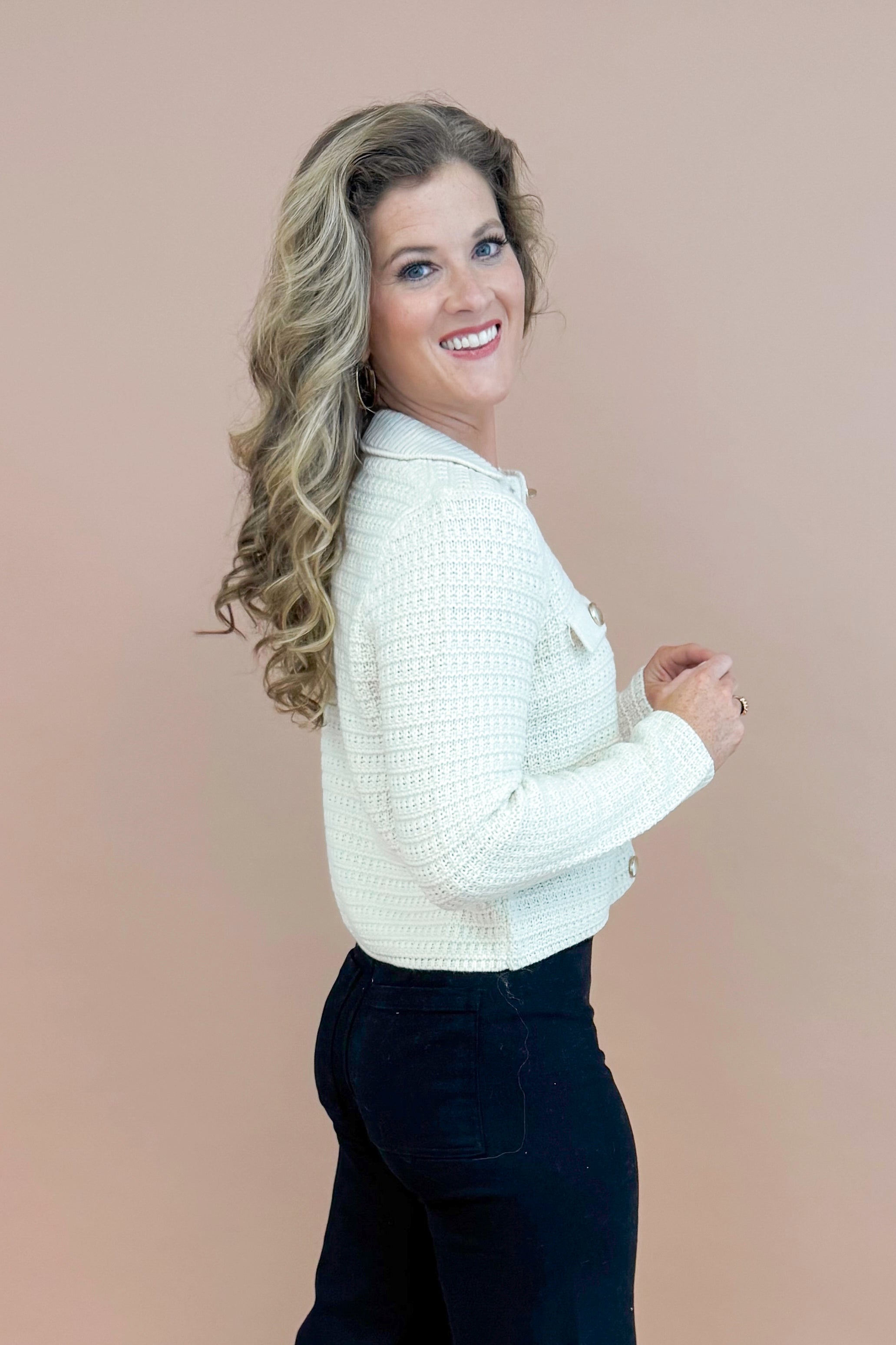 Side view of woman wearing Cream Textured Button Up Cardigan and jeans with taupe background.