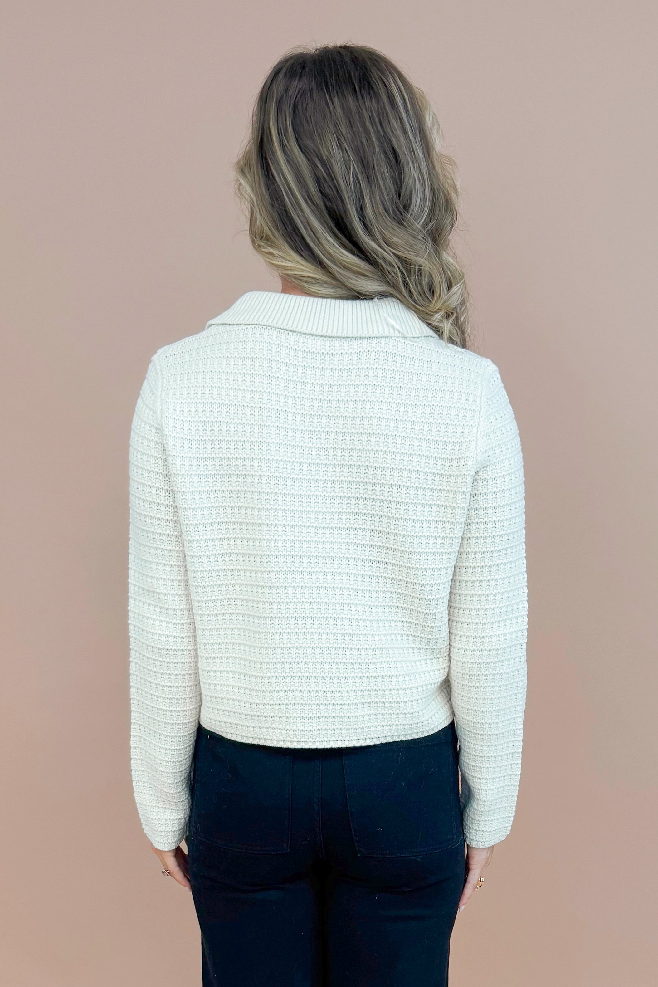 Back view of woman wearing Cream Textured Button Up Cardigan and jeans with taupe background.