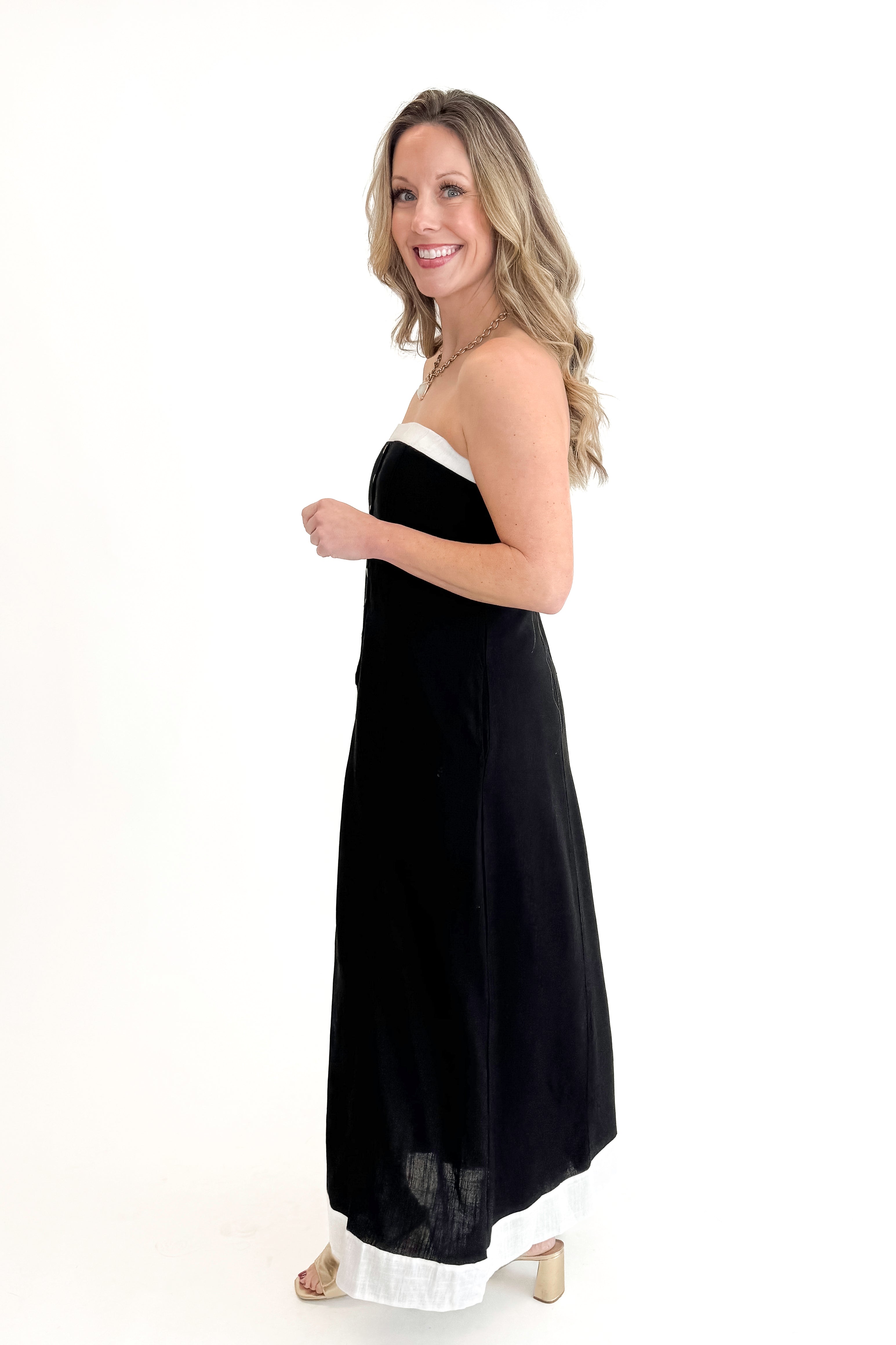 Side view of woman wearing Black With White Lining Button Down Strapless Dress against white studio background.