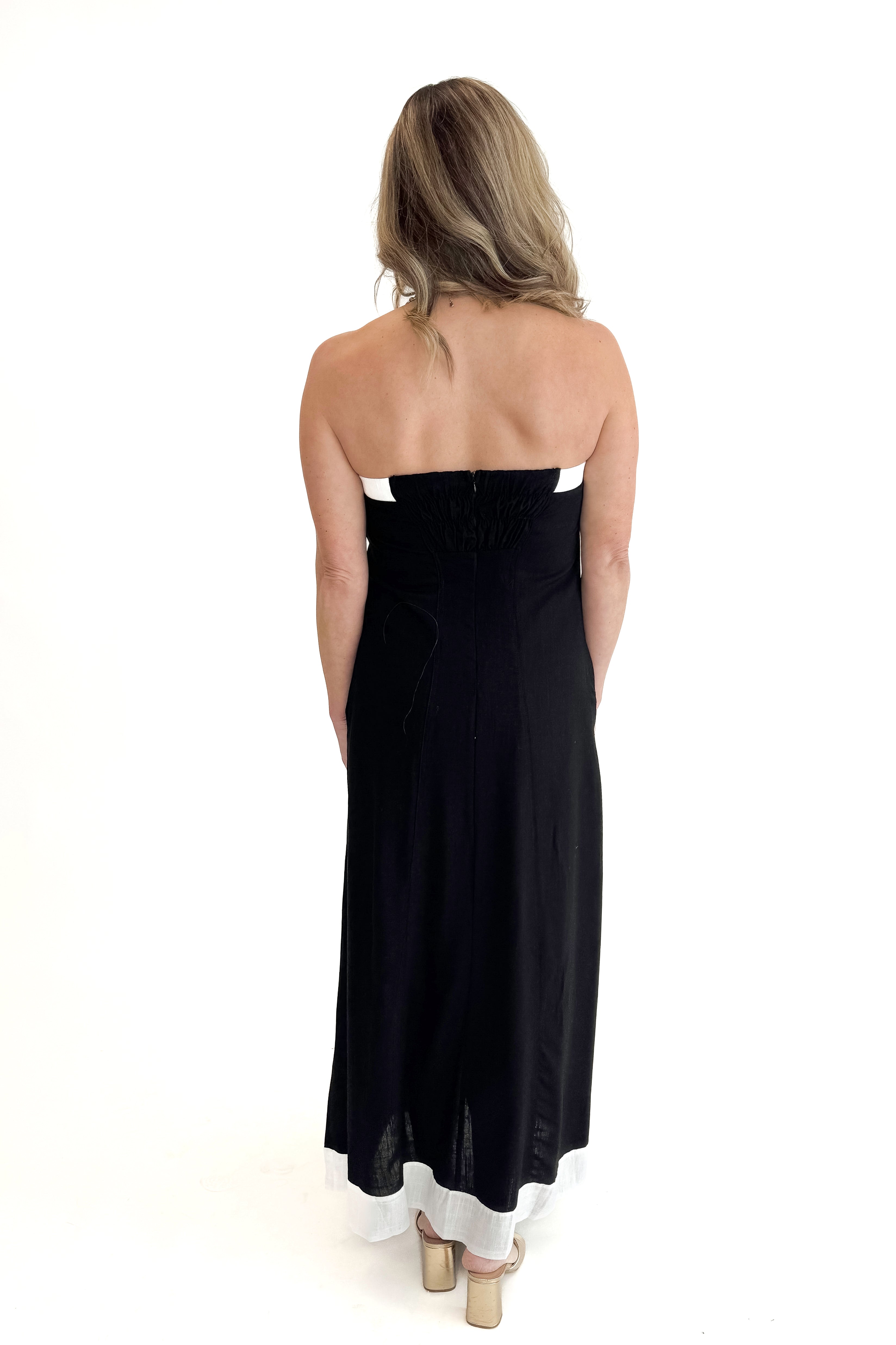 Back view of woman wearing Black With White Lining Button Down Strapless Dress against white studio background.