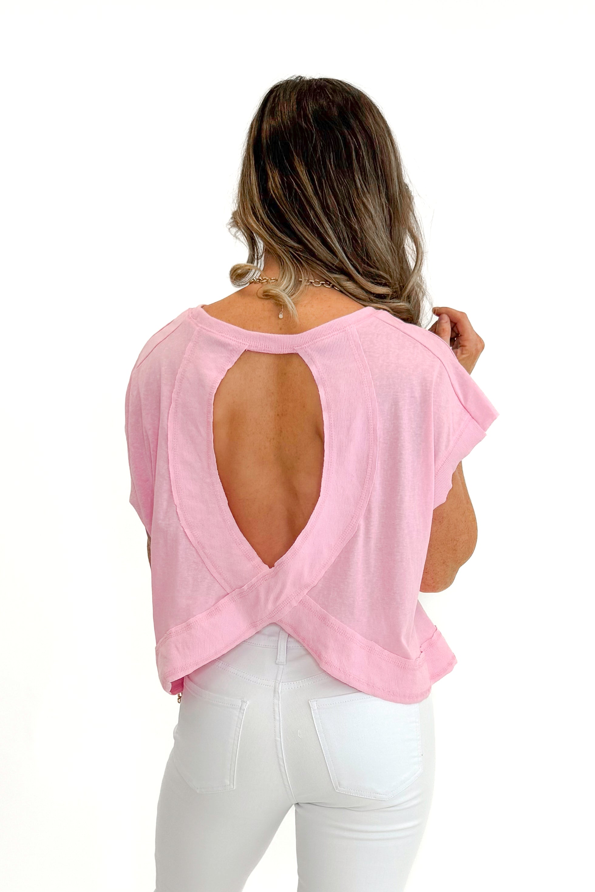 Back view of woman wearing Pink Cut Out Back Tee with jeans against white studio background.
