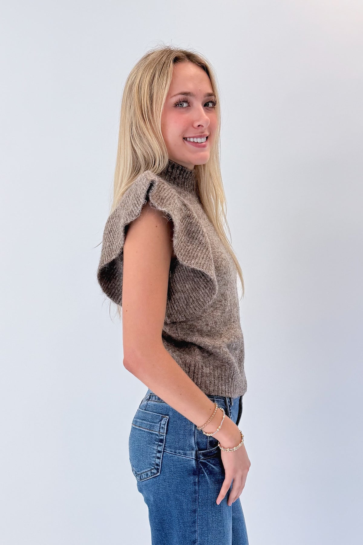 Side view of woman wearing Swagger Boutique’s Heathered Taupe Short Flutter Sleeve Sweater by Entro with jeans against white studio background.