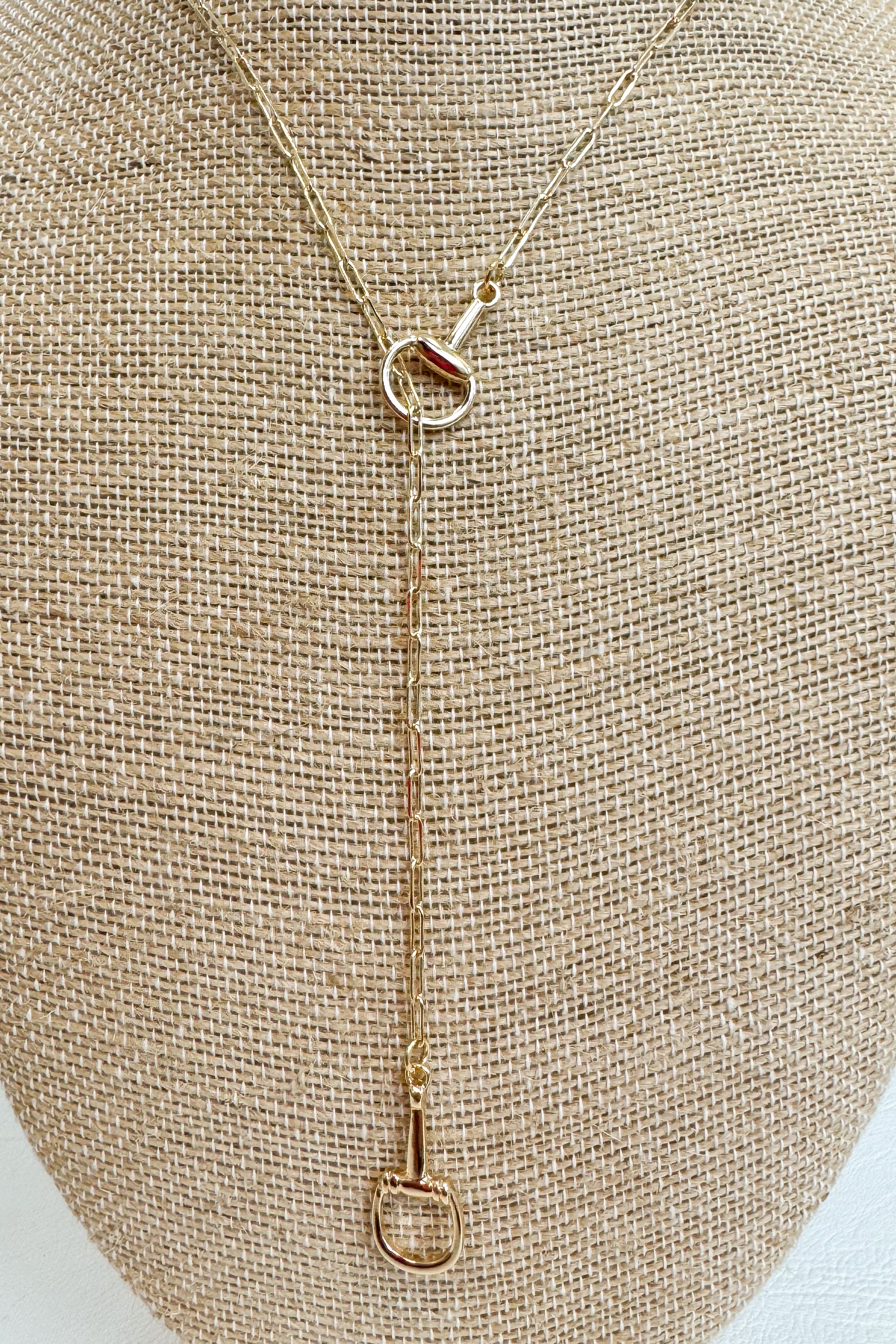 Gold-tone delicate chain necklace featuring a small horsebit pendant, displayed on a beige jewelry bust