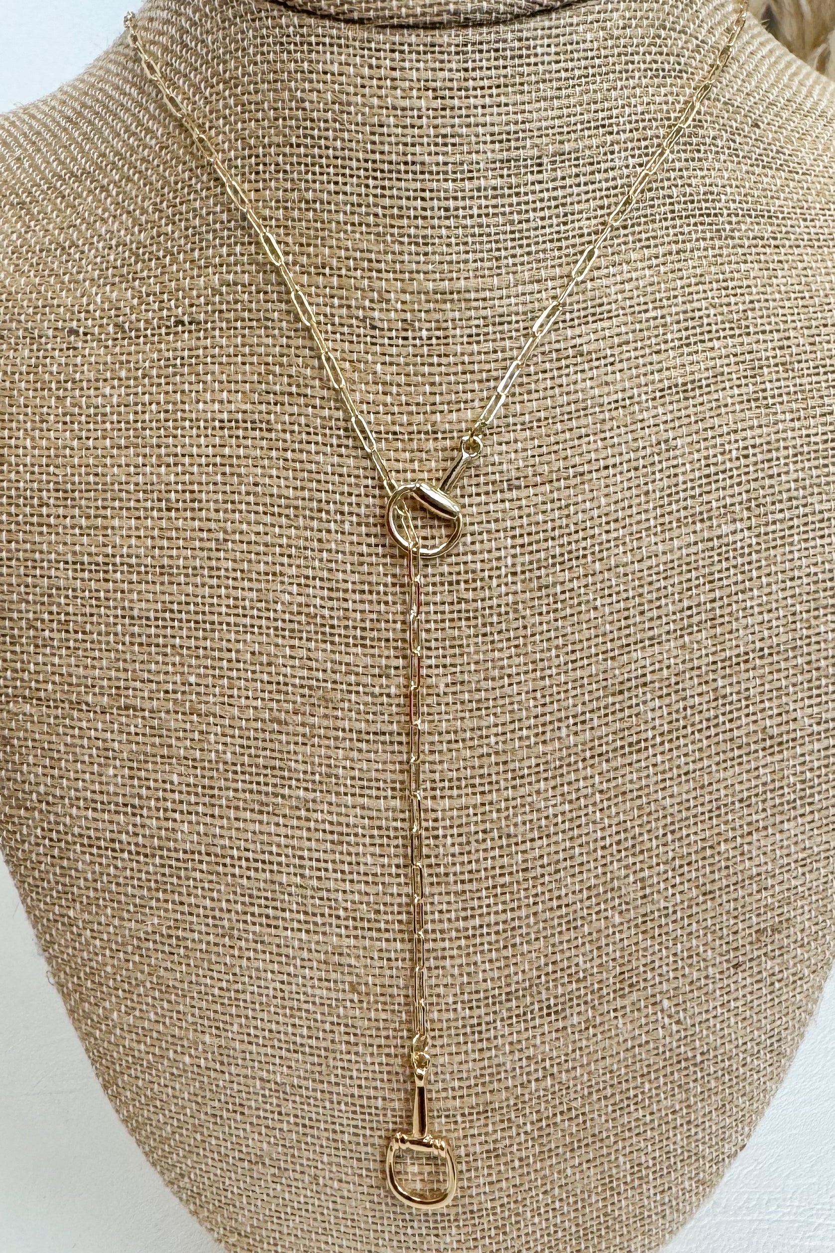 Gold-tone delicate chain necklace featuring a small horsebit pendant, displayed on a beige jewelry bust against a white studio background