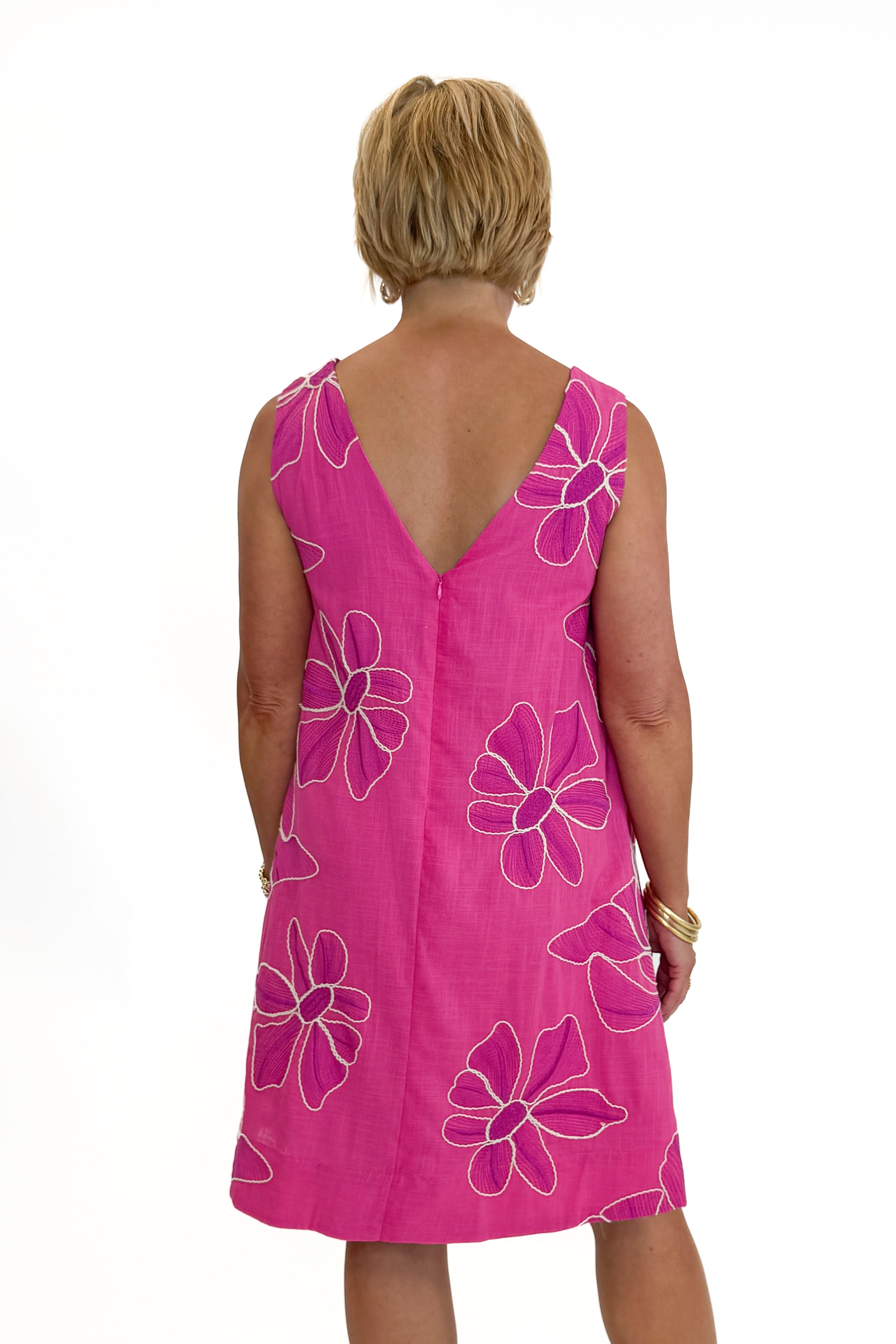 Back view of woman wearing Swagger Boutique’s Hot Pink Floral Embroidered Mini Dress with heels against white studio background.