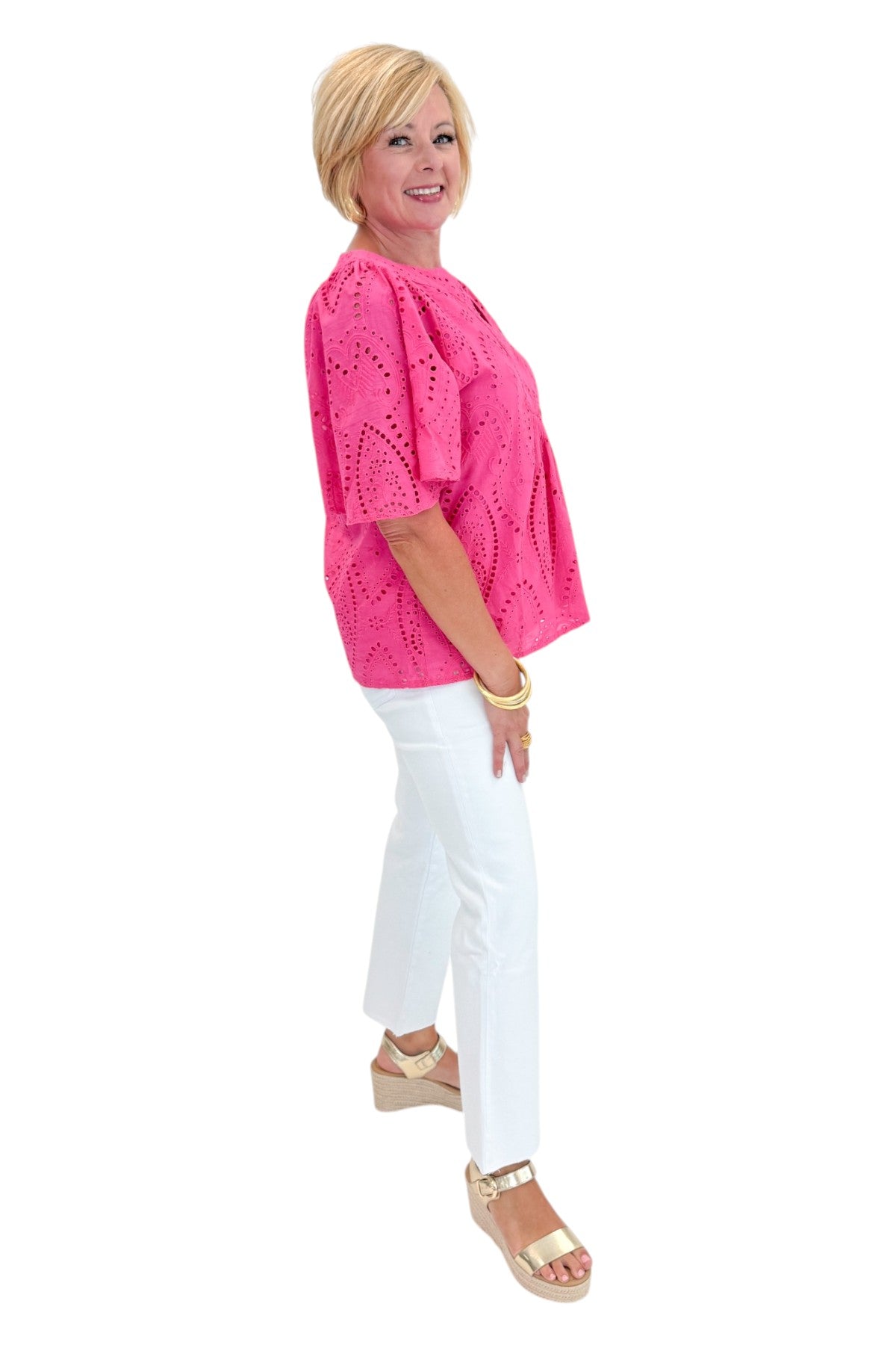 Side view of woman wearing Swagger Boutiqueās Hot Pink Flutter Sleeve Eyelet Top with jeans against white studio background.