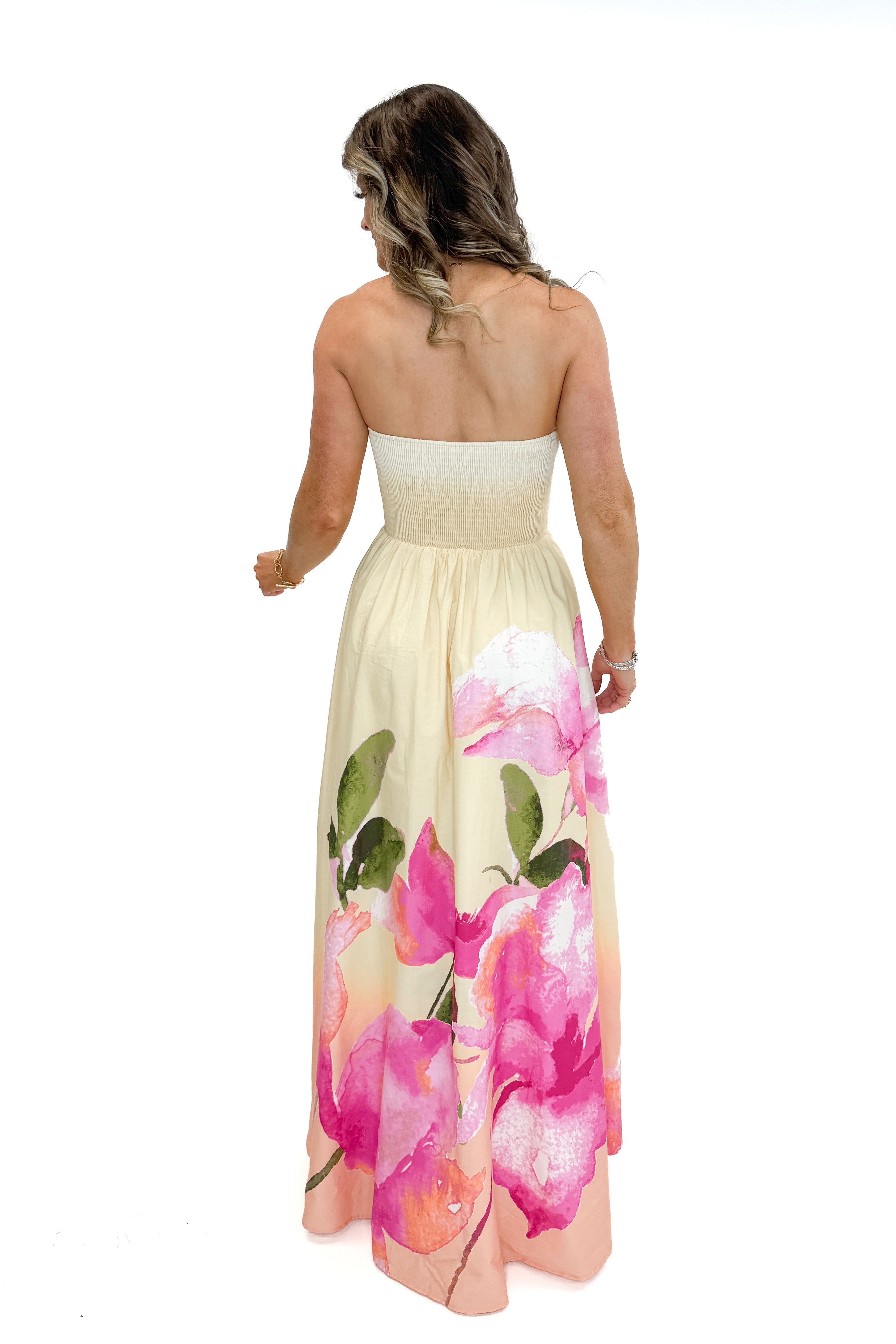 Back view of woman wearing Yellow & Pink Floral Print Strapless Maxi Dress against white studio background.