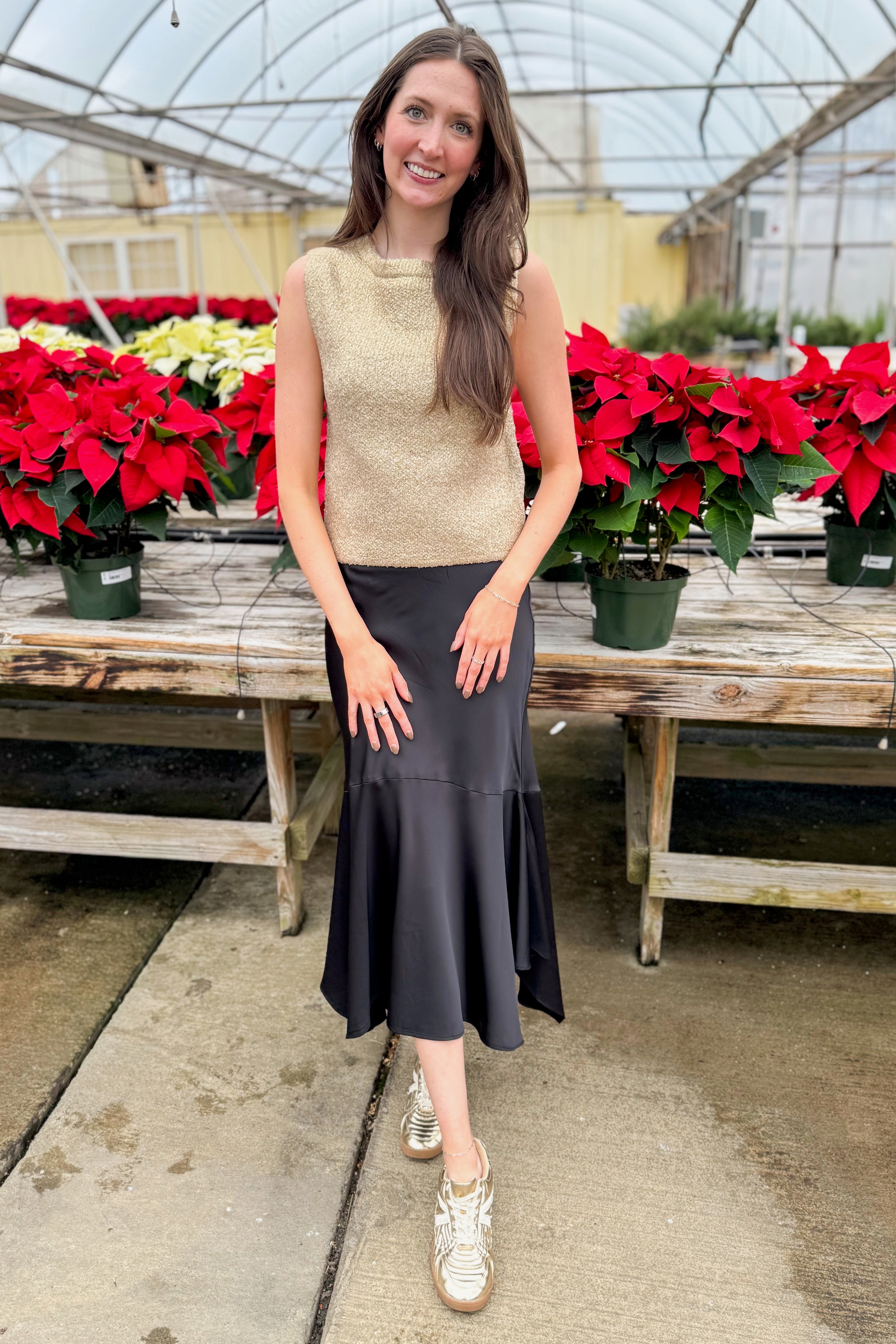 Front view of woman wearing Gold Sleeveless Sweater with skirt by holiday decor.