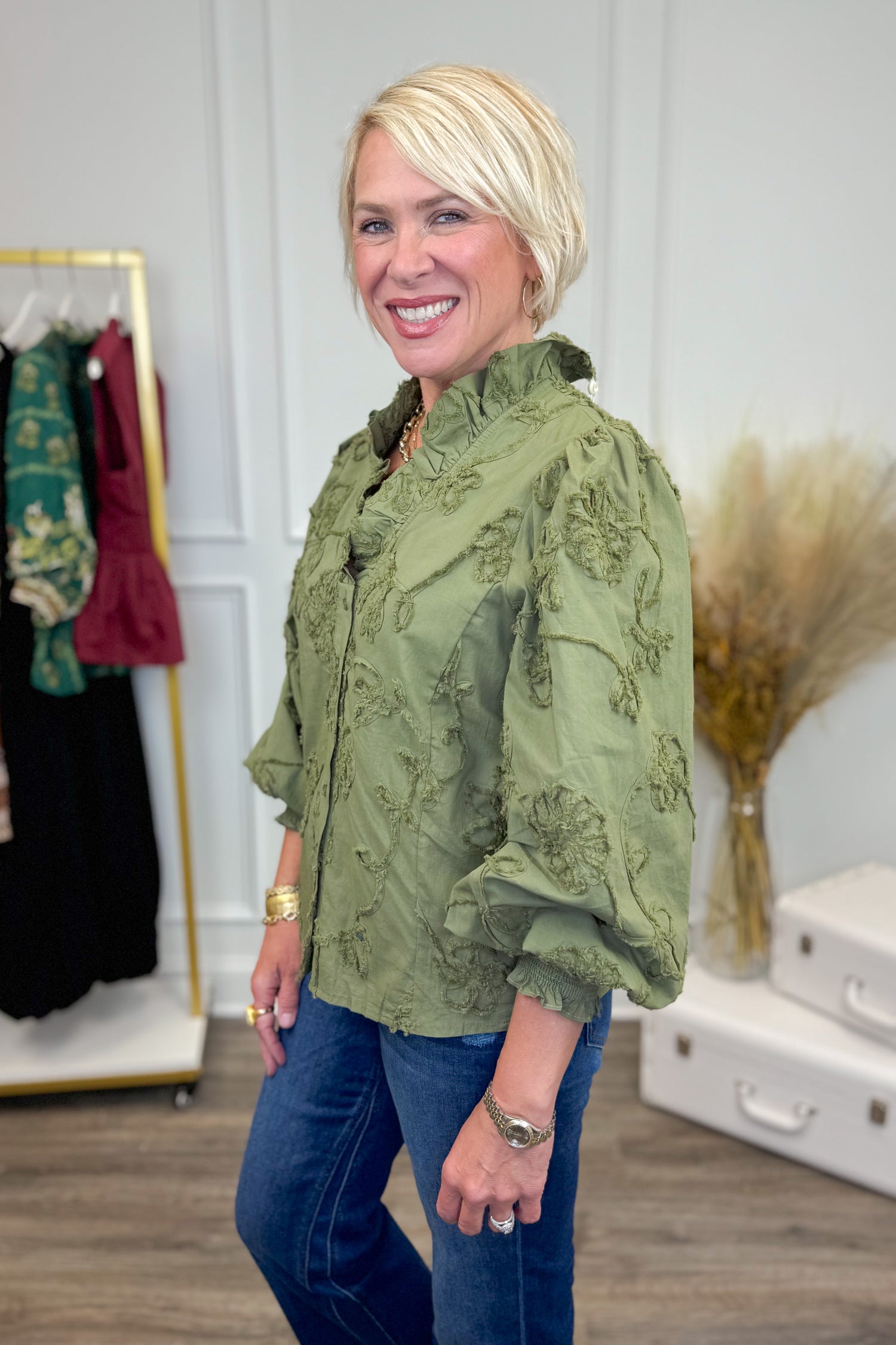 Woman wearing Pick Me Olive Floral Applique Ruffle Detail Top - side view showing floral applique design and ruffle detailing in olive green