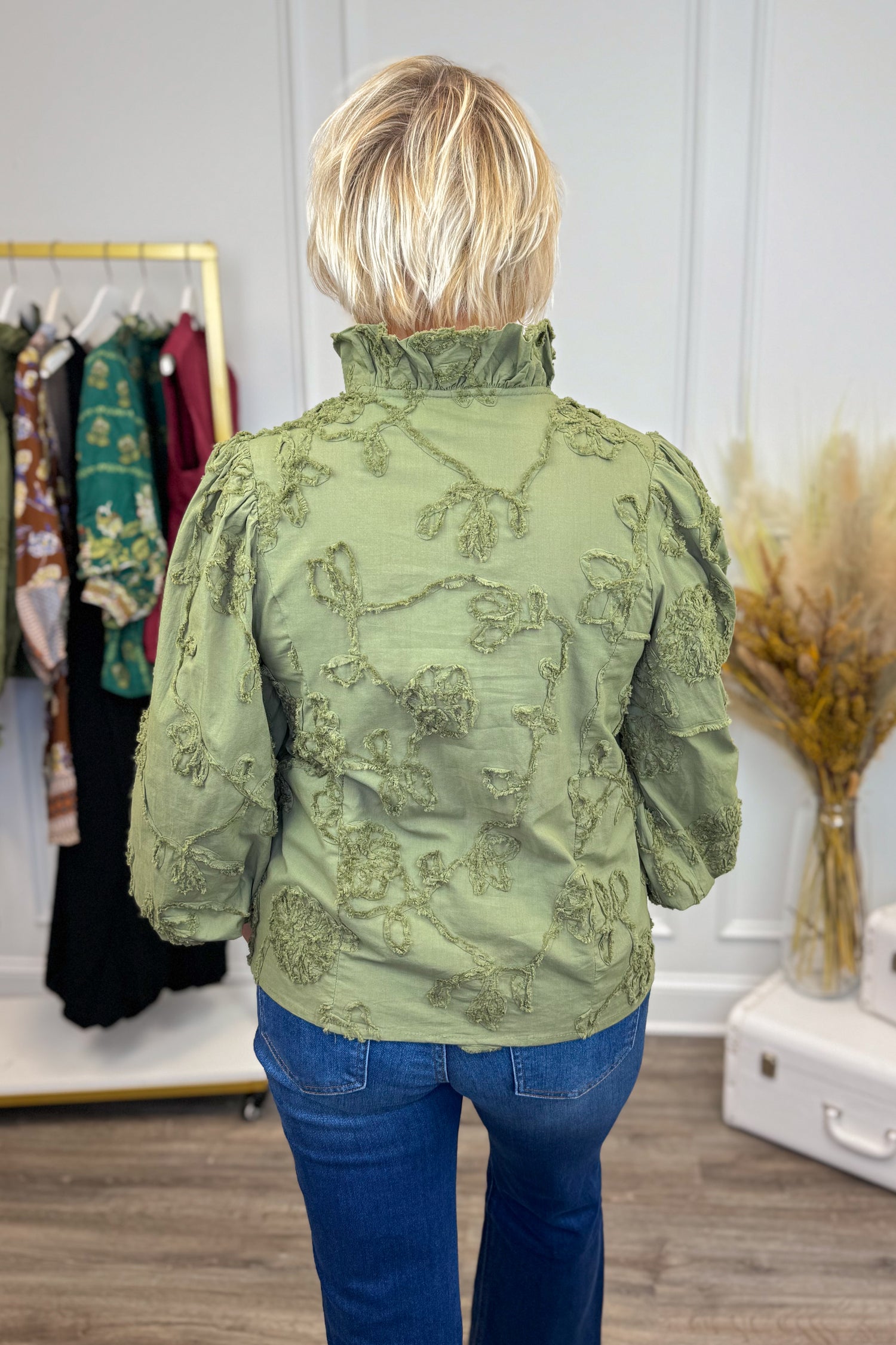 Woman wearing Pick Me Olive Floral Applique Ruffle Detail Top - back view showing floral applique design and ruffle detailing in olive green