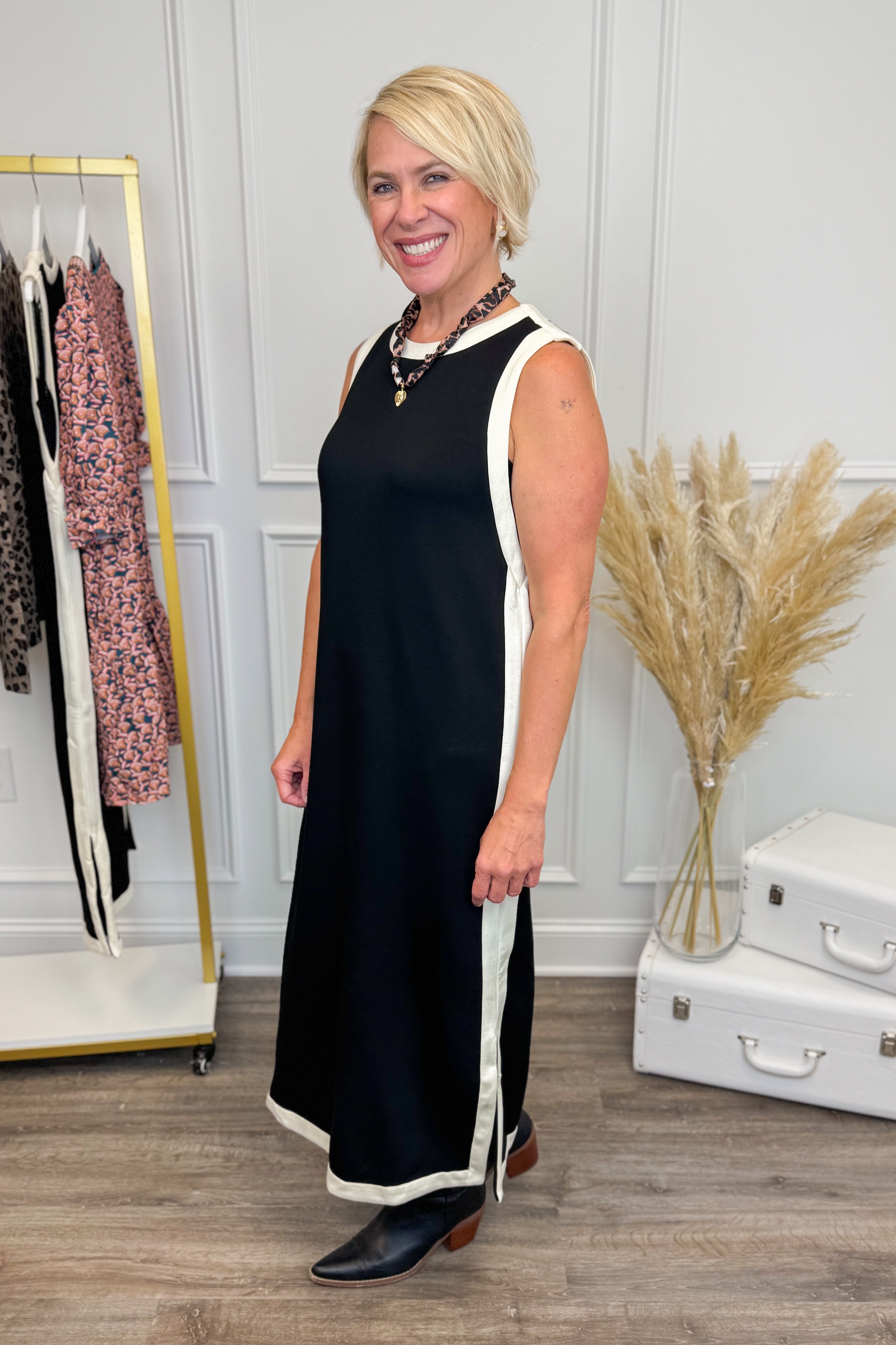 Side picture of woman wearing Black With Cream Lining Midi Dress by Entro with clothes in the background.
