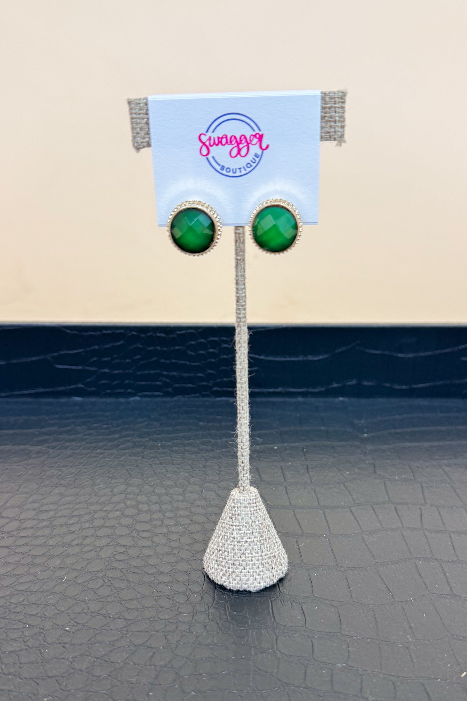 Green earrings on a stand with a branded card in the background
