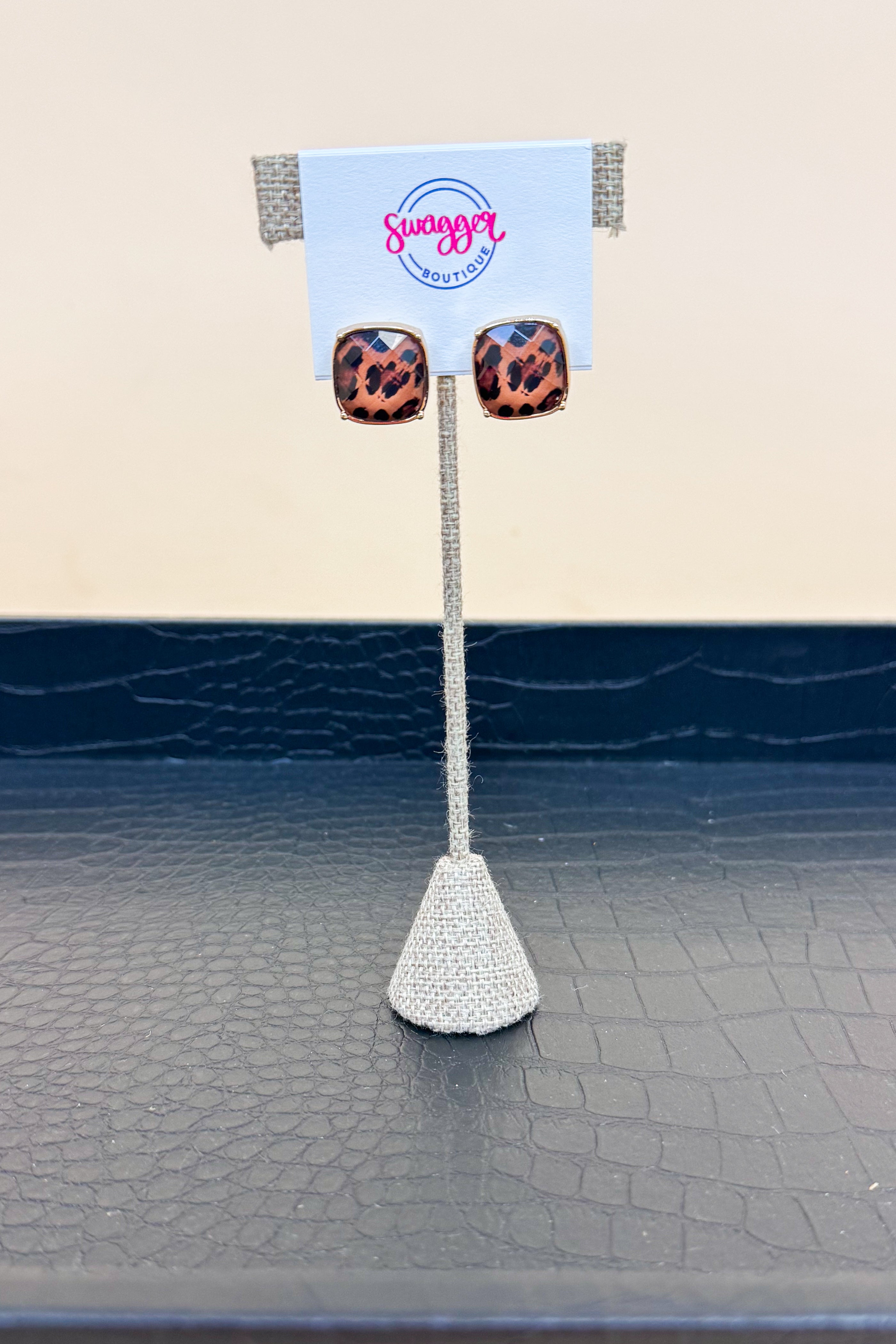Pair of leopard print earrings on a stand with a &