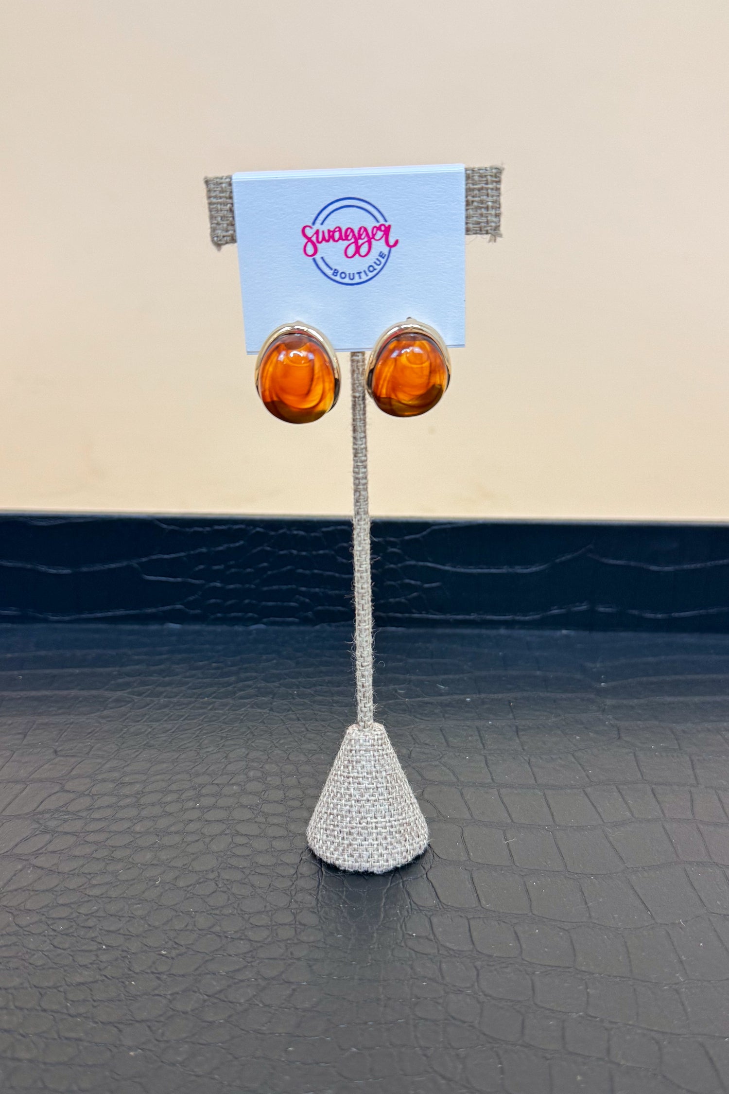 Pair of amber earrings on a stand with a branded card against a beige and black background