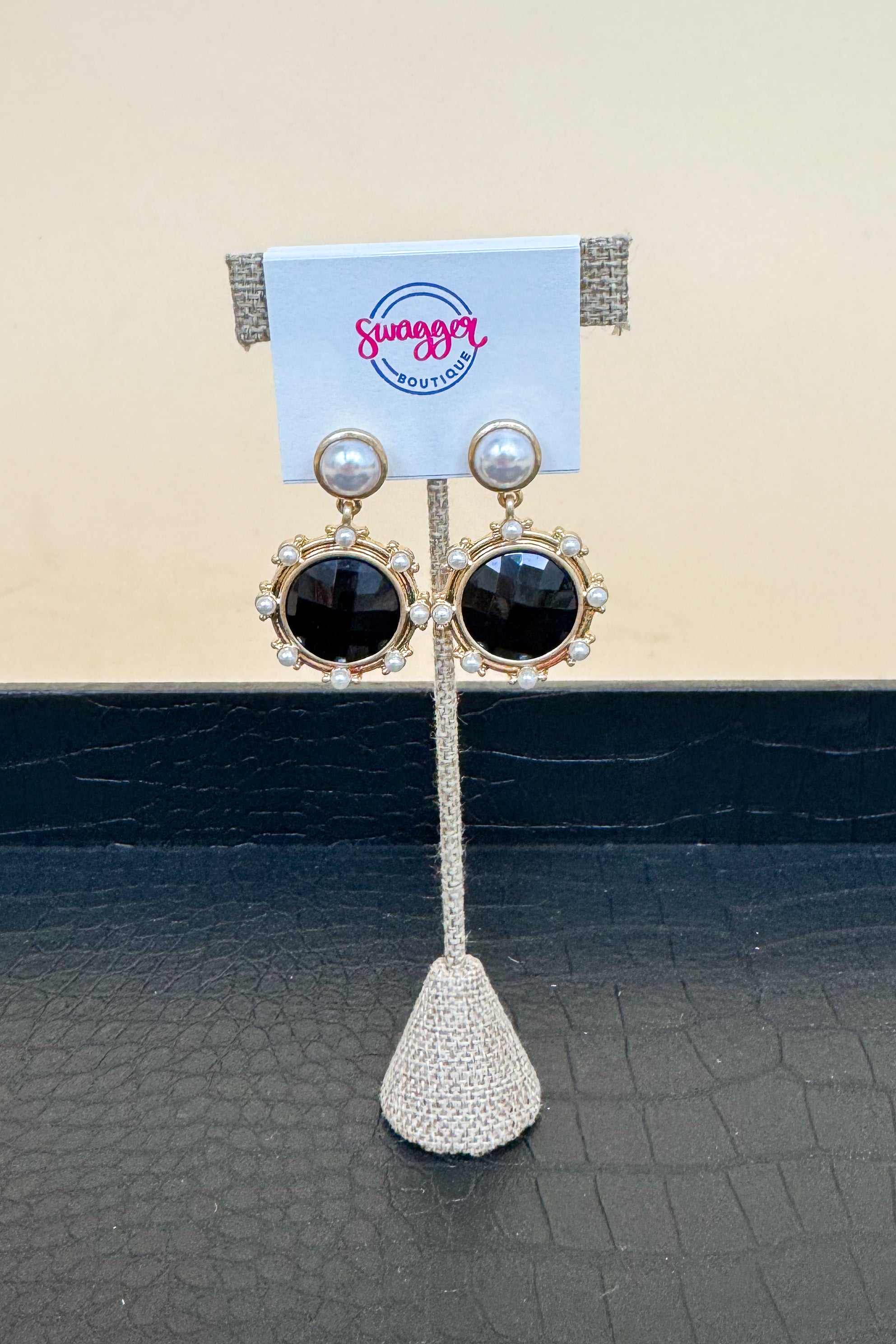 Pair of earrings on a display stand with a brand card in the background.