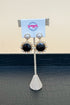 Pair of earrings on a display stand with a brand card in the background.