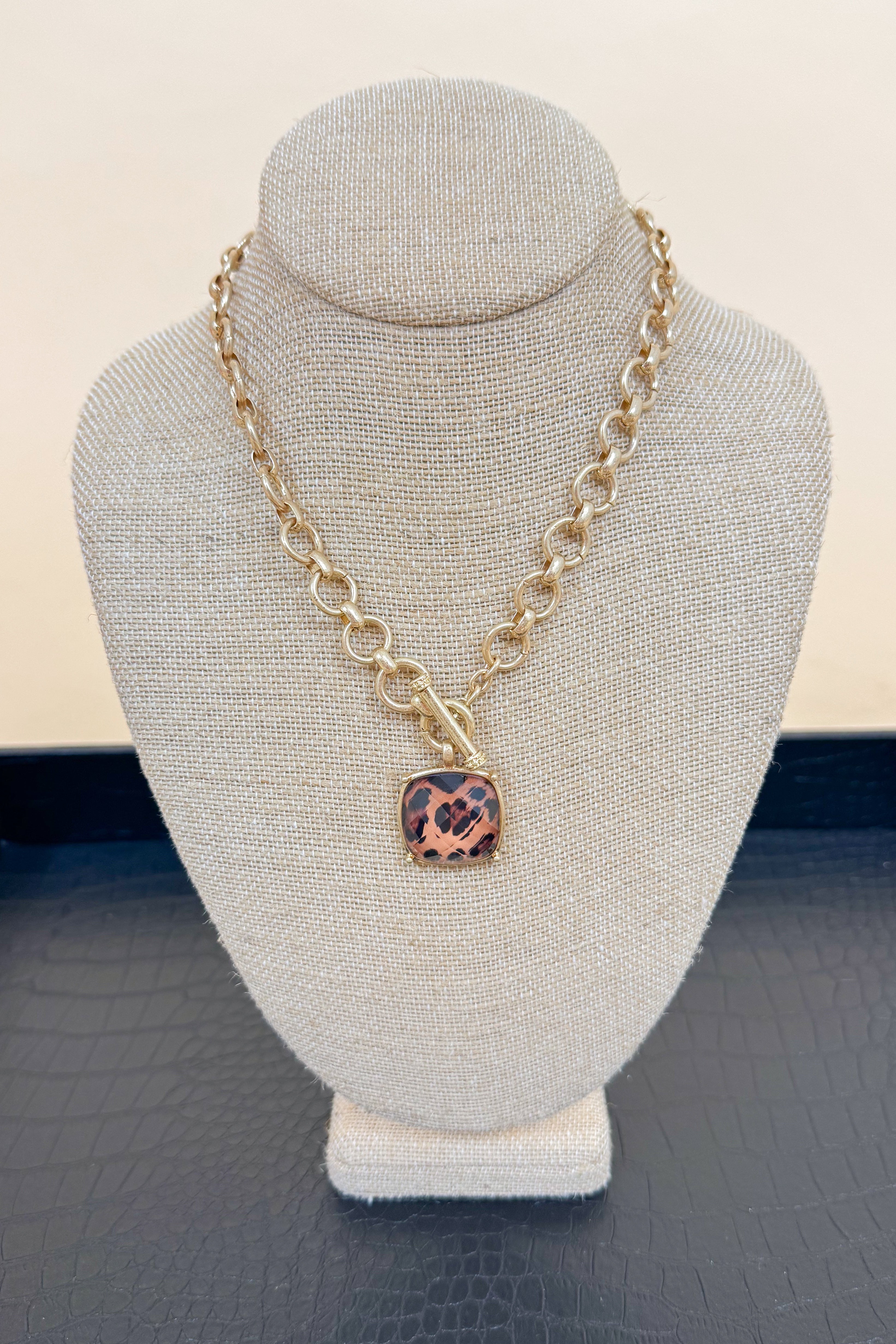 Gold chain necklace with a leopard print pendant on a gray bust