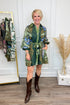 Woman wearing a green patterned dress with brown boots in a room with decor elements.