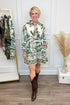Woman wearing a floral dress and brown boots in a room with a white wall and wooden floor.
