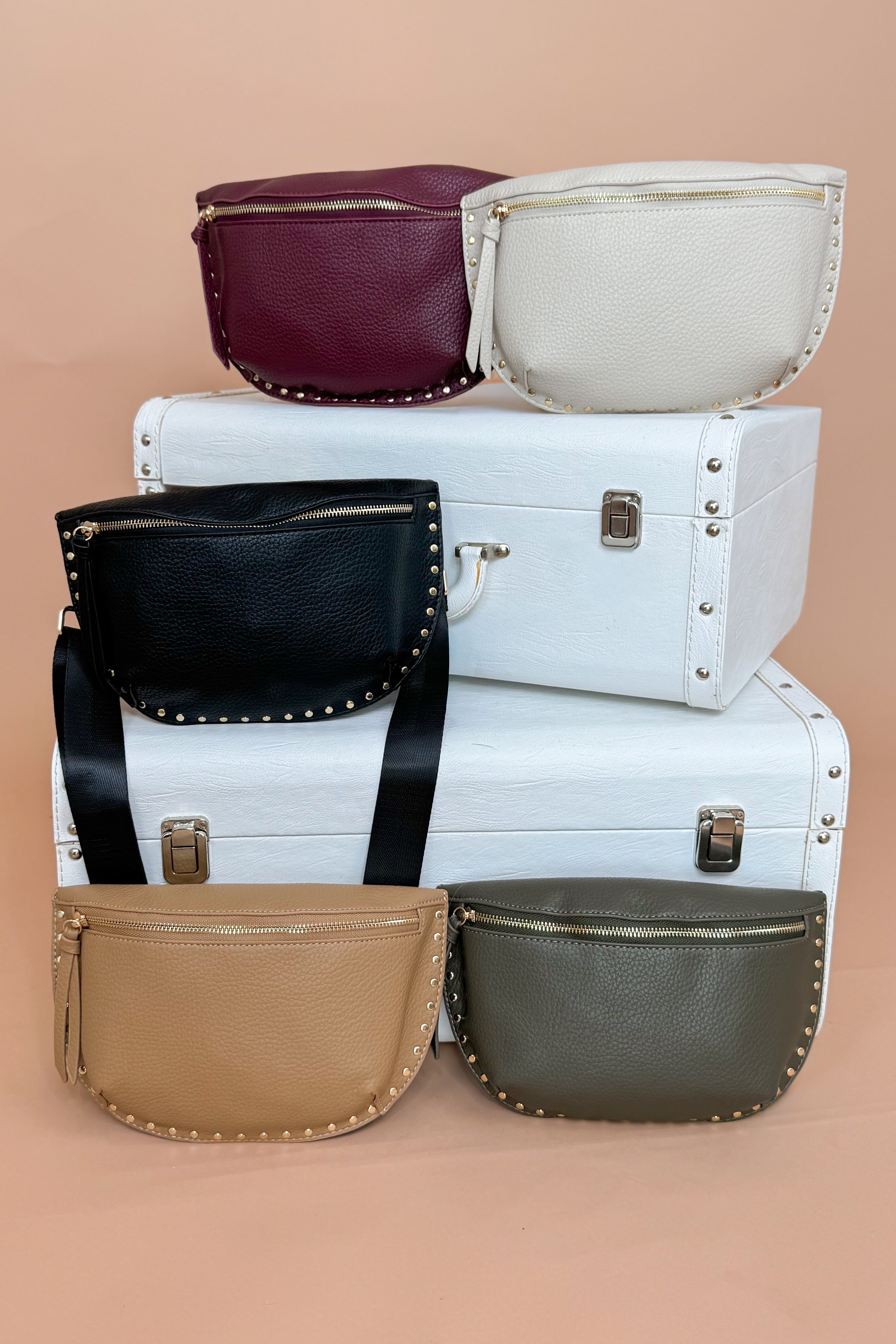 Stack of white suitcases with various colored handbags on top against a beige background