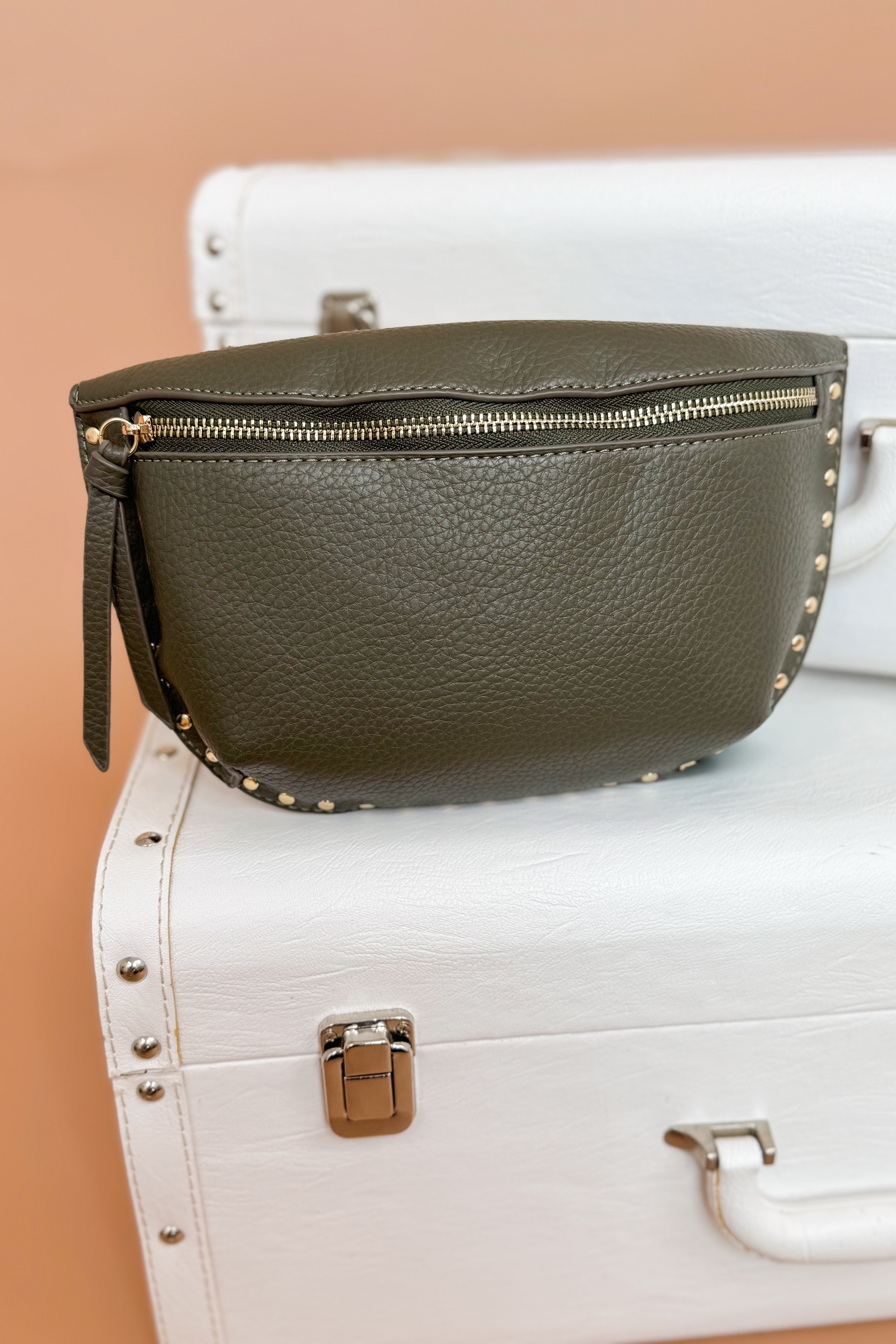 Green leather clutch bag with gold accents on a white suitcase