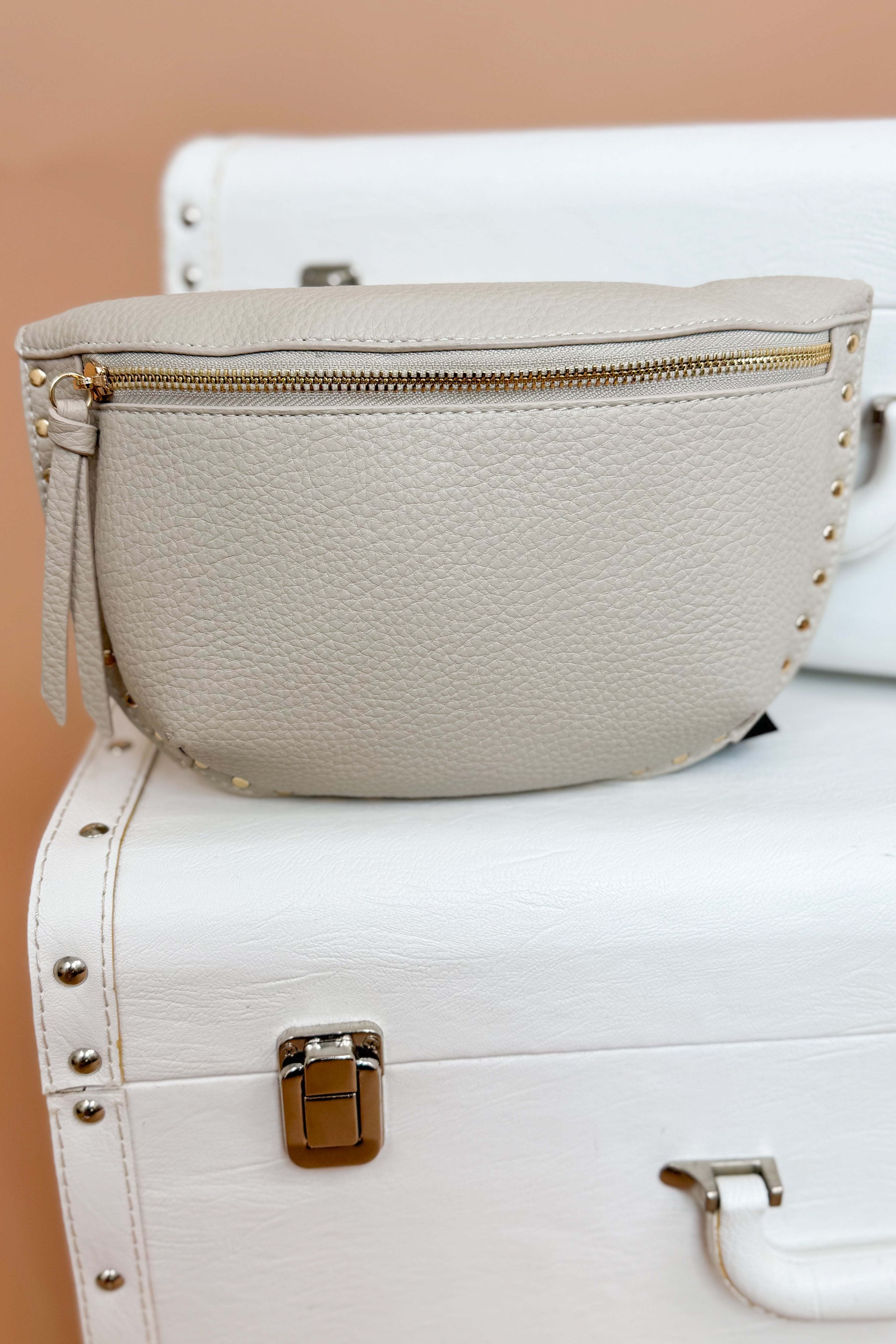Beige leather bag with gold zipper on a white suitcase against a beige background