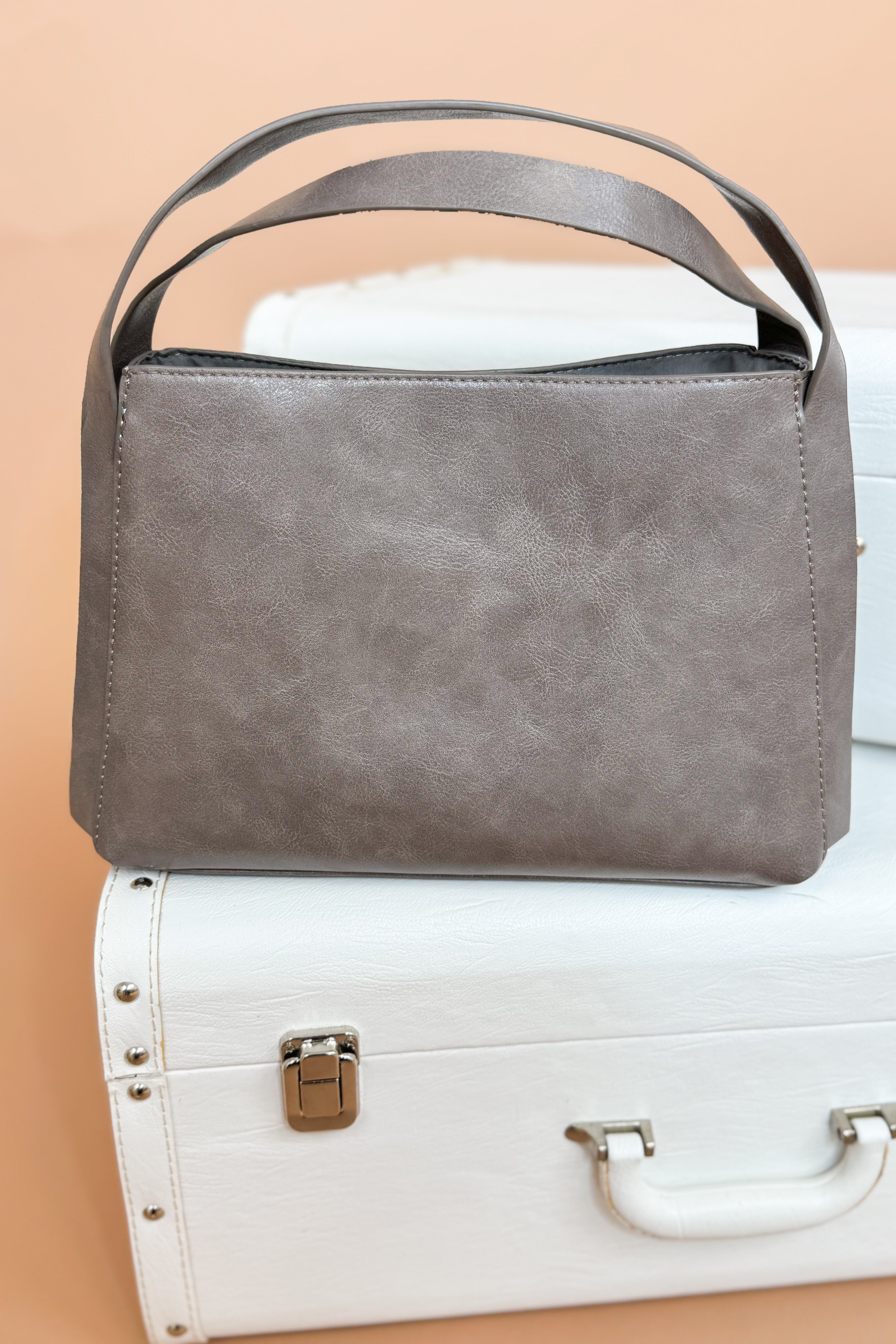 Gray handbag on a white suitcase with a beige background