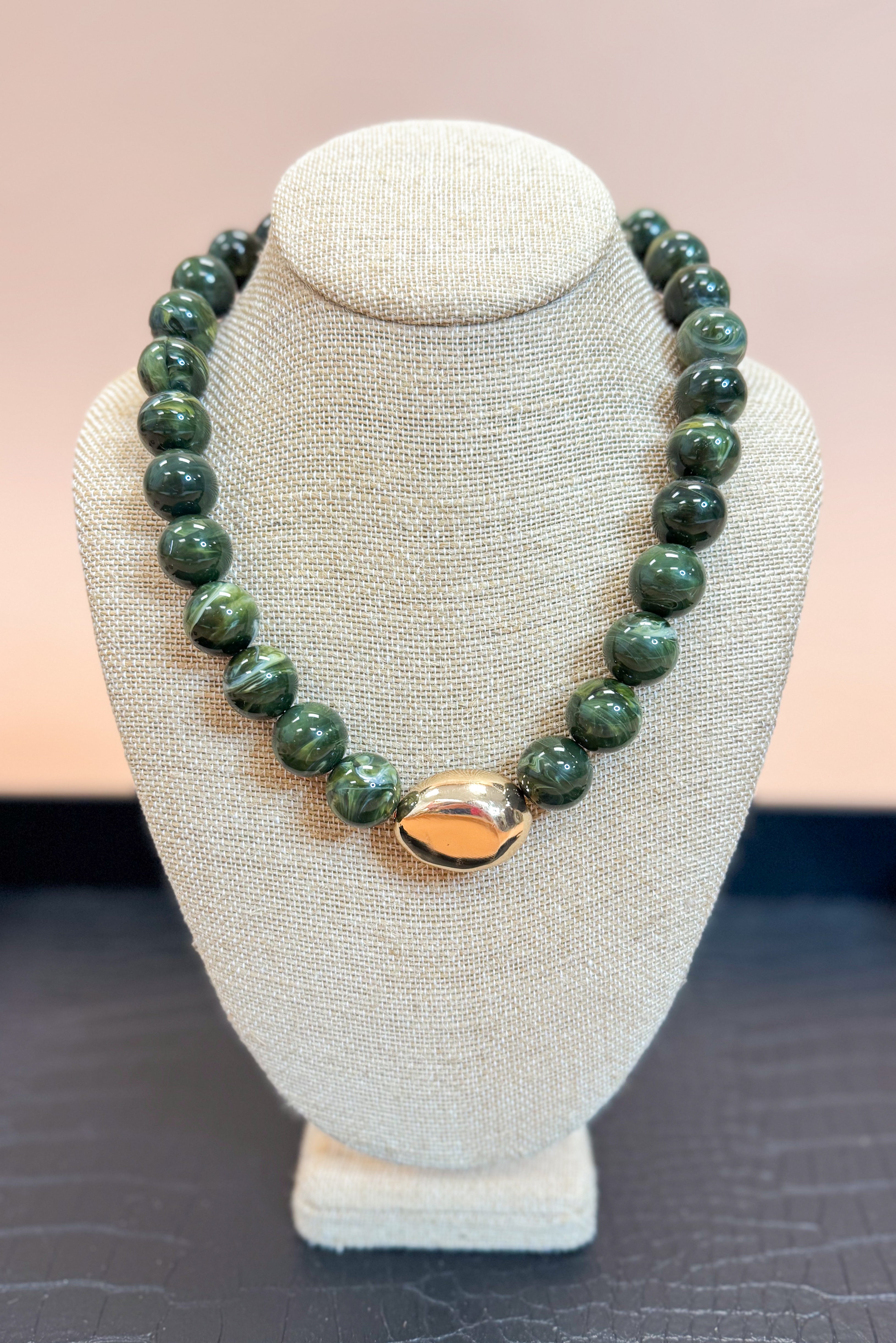 Green beaded necklace with a gold clasp on a gray bust