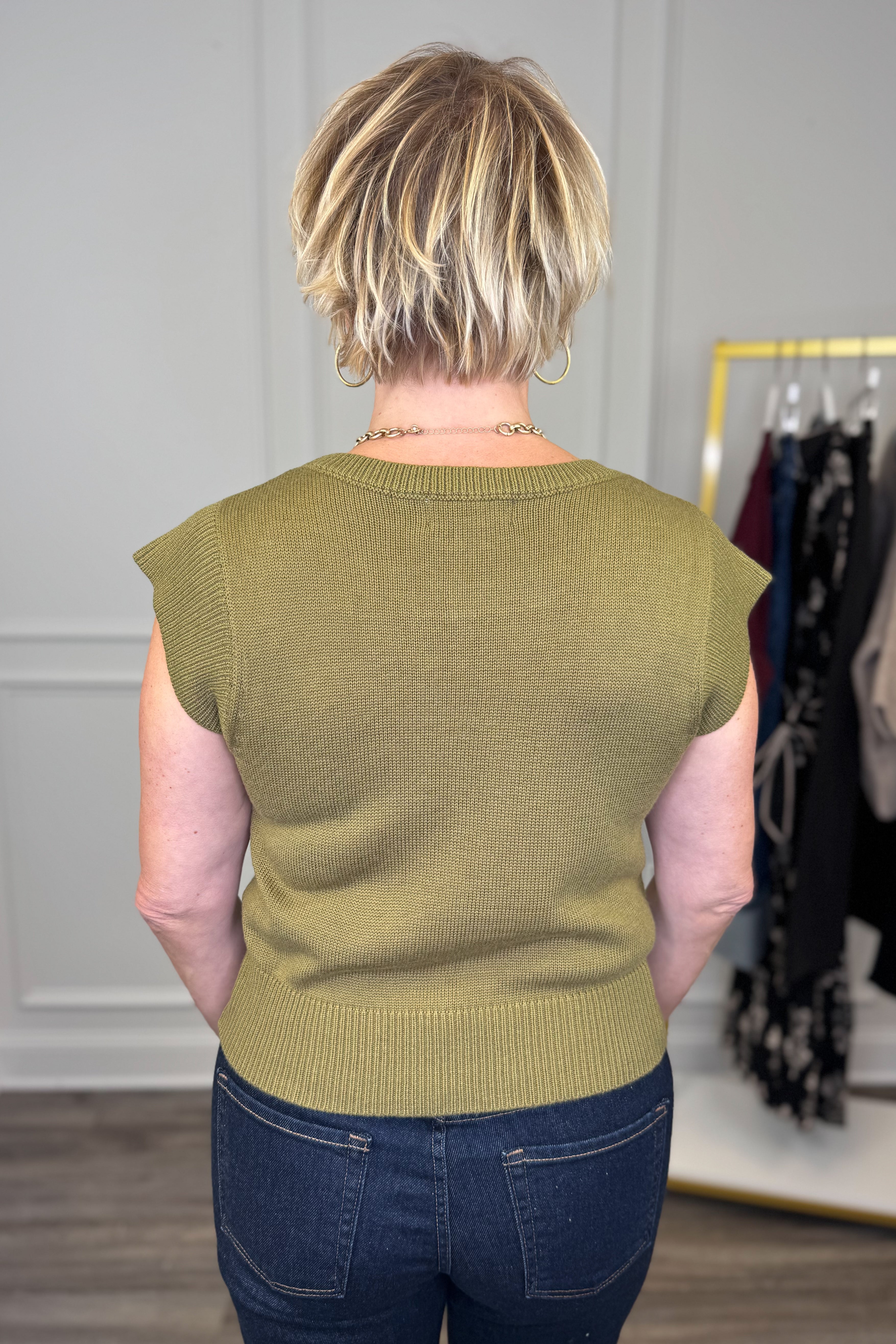 Person wearing a green sleeveless sweater in an indoor setting